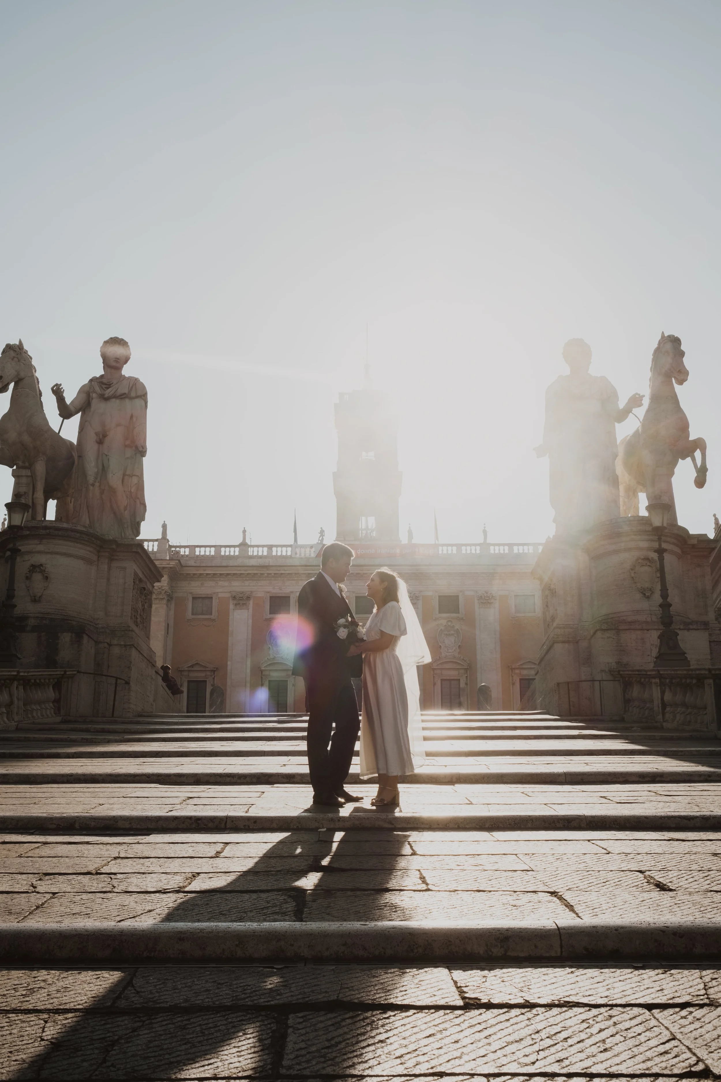 Couple standing together at sunrise on Capitoline Hill in Rome during an intimate elopement, backlit by soft sunlight