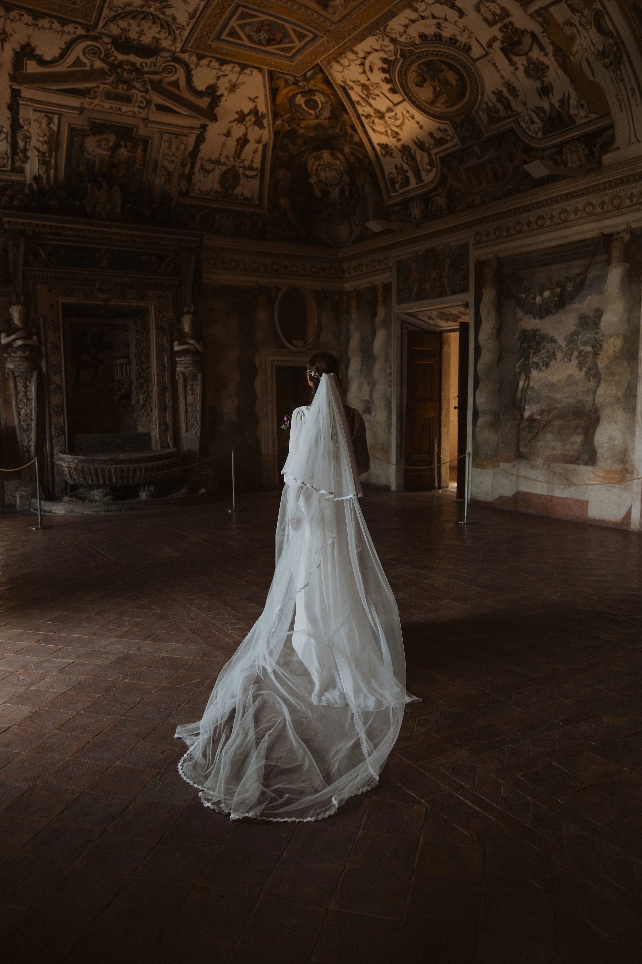Bride wearing a long veil standing inside a historic Roman villa with frescoed ceilings during an intimate elopement