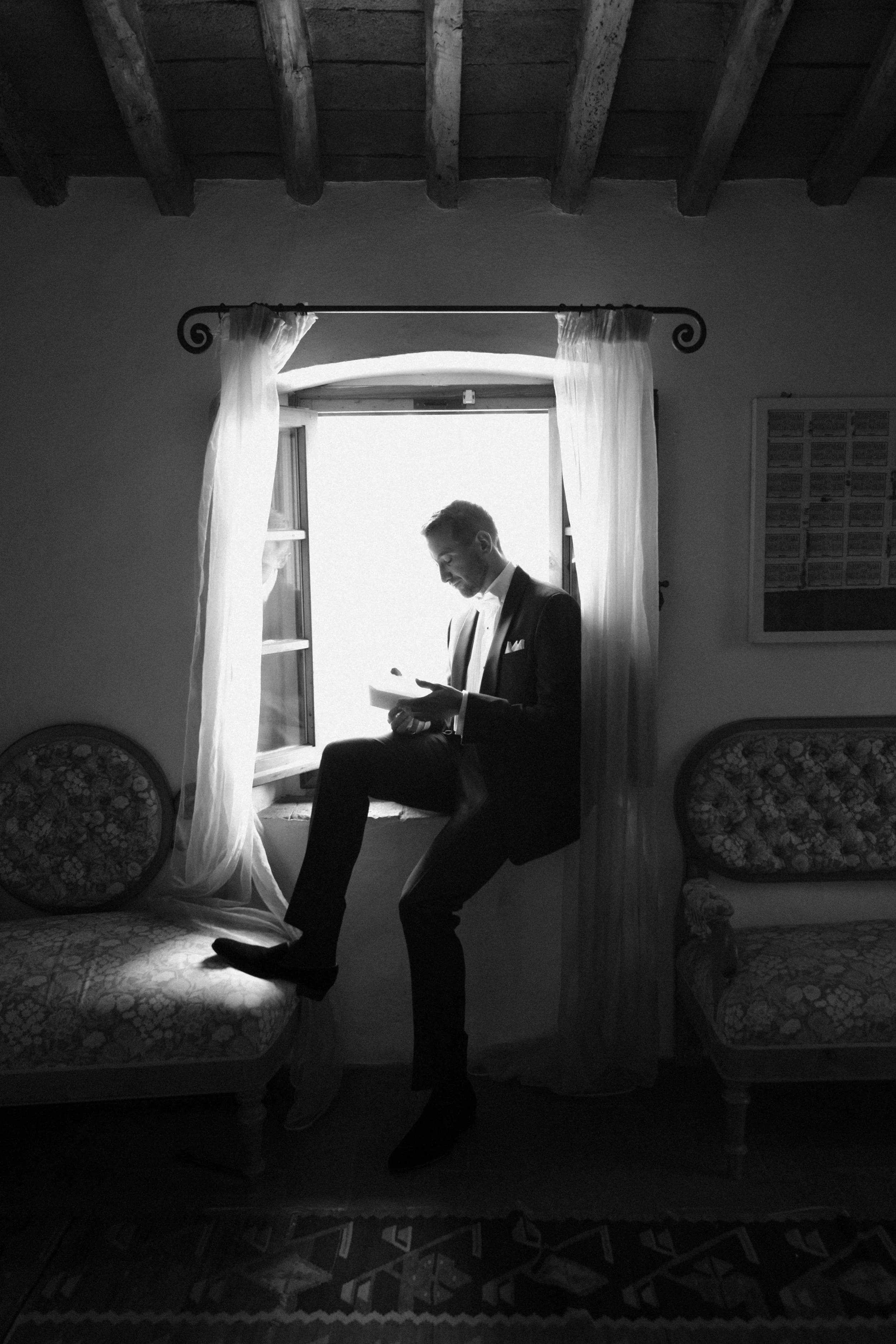 An intimate pre-ceremony moment at Castello di Bibbione in Tuscany, capturing the groom reading a handwritten letter by the window. A timeless, documentary-style image reflecting quiet emotion, refined elegance, and the atmosphere of a luxury destina