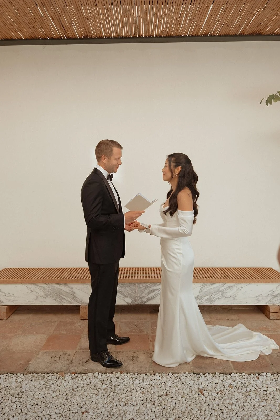 The couple stand together during their wedding ceremony inside Villa Lena, photographed in a minimalist space filled with natural light and soft shadows.