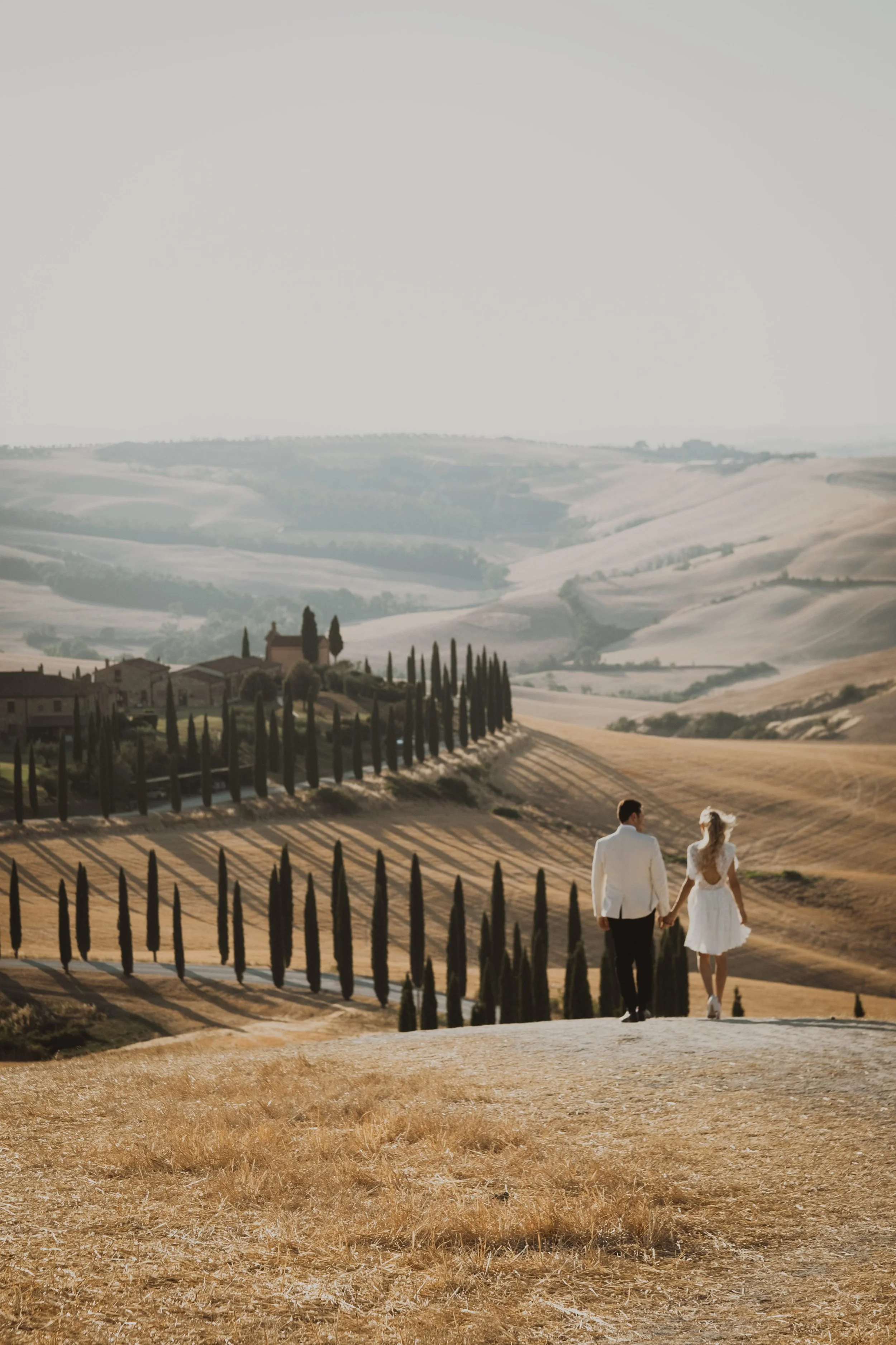 Couple walking through the Val d’Orcia hills, an iconic Tuscany backdrop for a romantic and refined destination wedding.