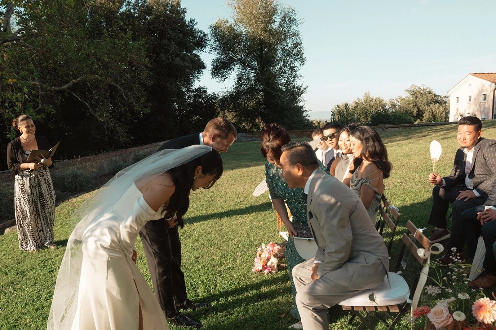 The bride and groom bow together to greet family members after the ceremony, captured in warm afternoon light on the Tuscan lawn.