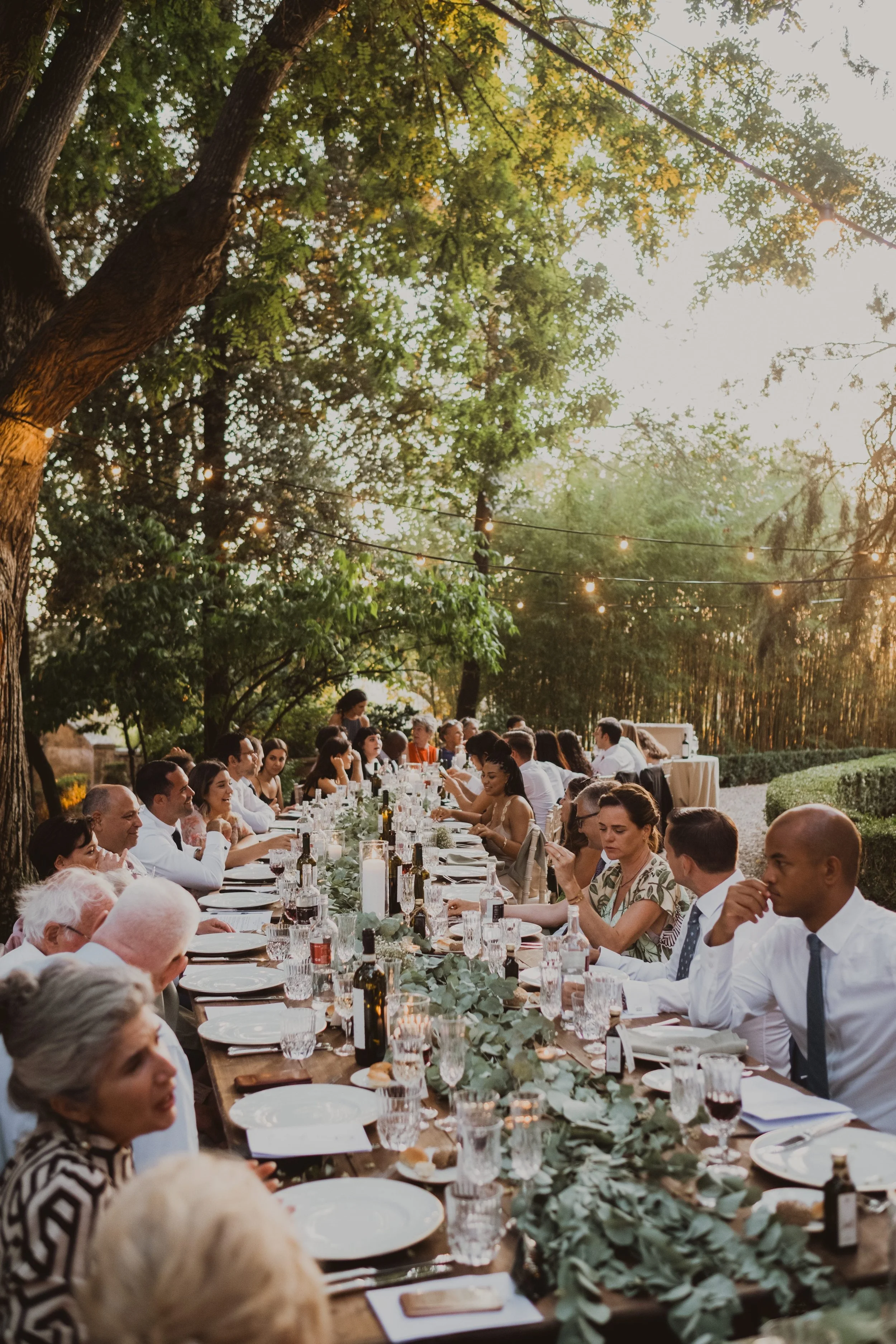 Long table wedding dinner under trees with soft lighting and natural styling, creating an intimate luxury wedding atmosphere in Italy.