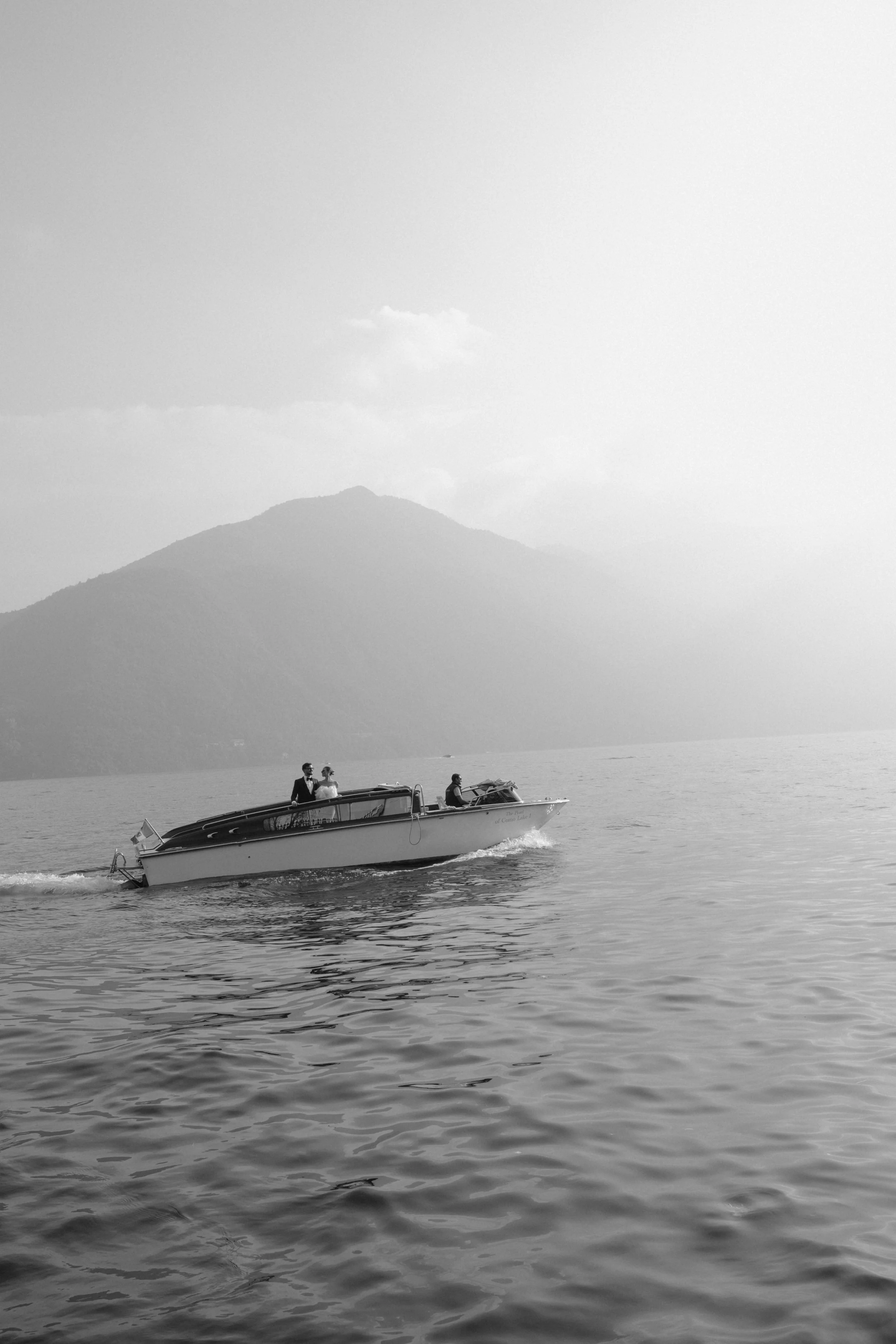 A bride and groom cruising across Lake Como by classic wooden boat, photographed near Villa Balbiano. A refined, editorial wedding moment capturing timeless Italian elegance, cinematic light, and the quiet luxury of a Lake Como destination wedding.