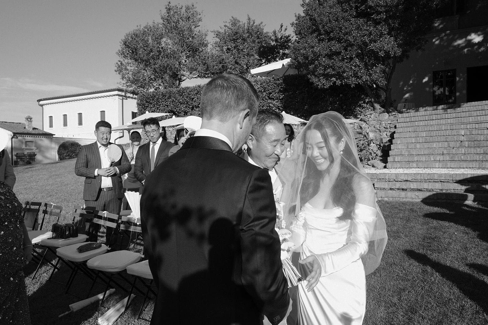An emotional black and white moment as the bride meets her family at the ceremony, captured among guests during the outdoor wedding in Tuscany.