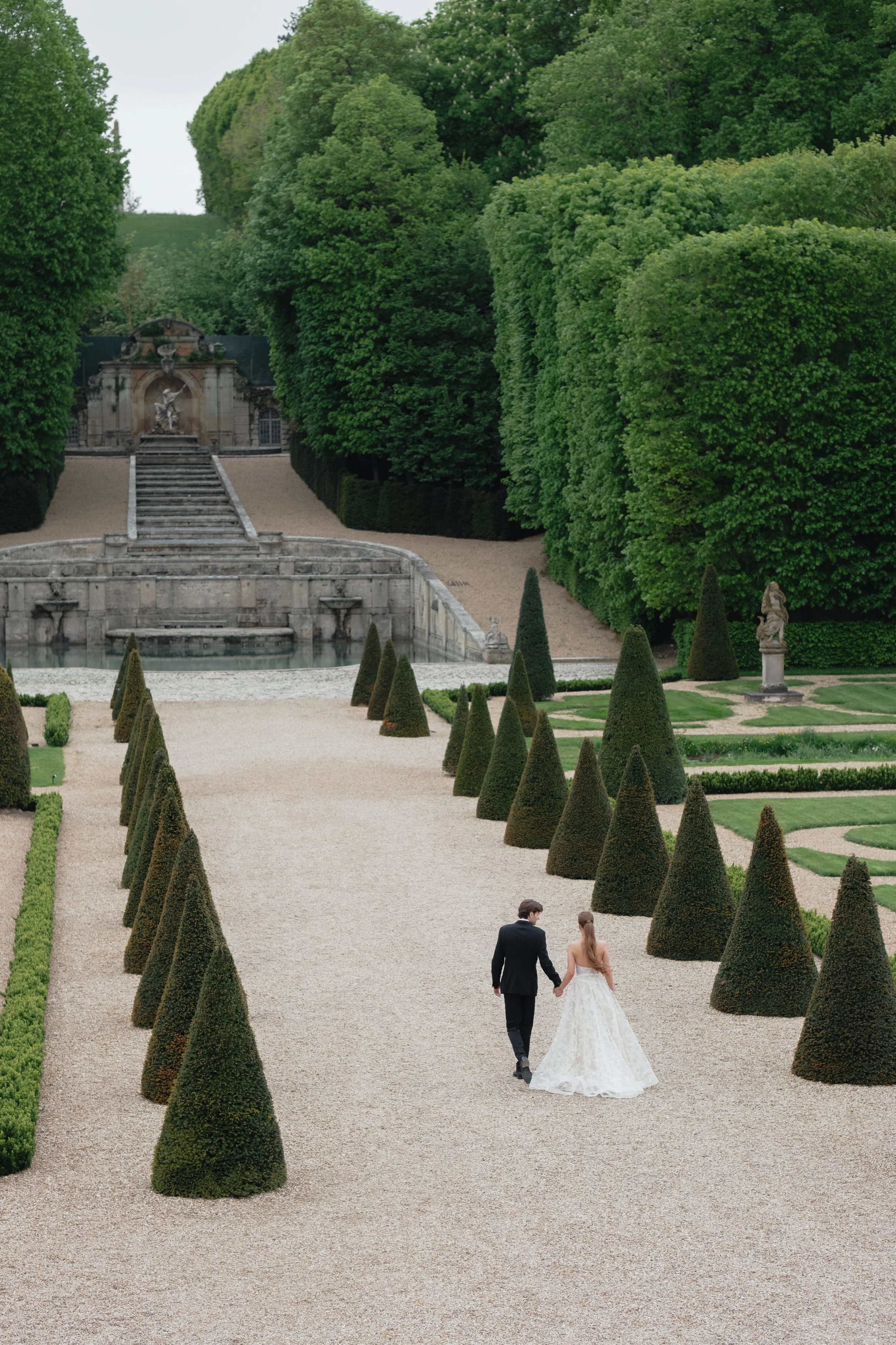 A wedding couple walking through the formal gardens of Château de Villette, photographed with a refined destination wedding style near Paris.