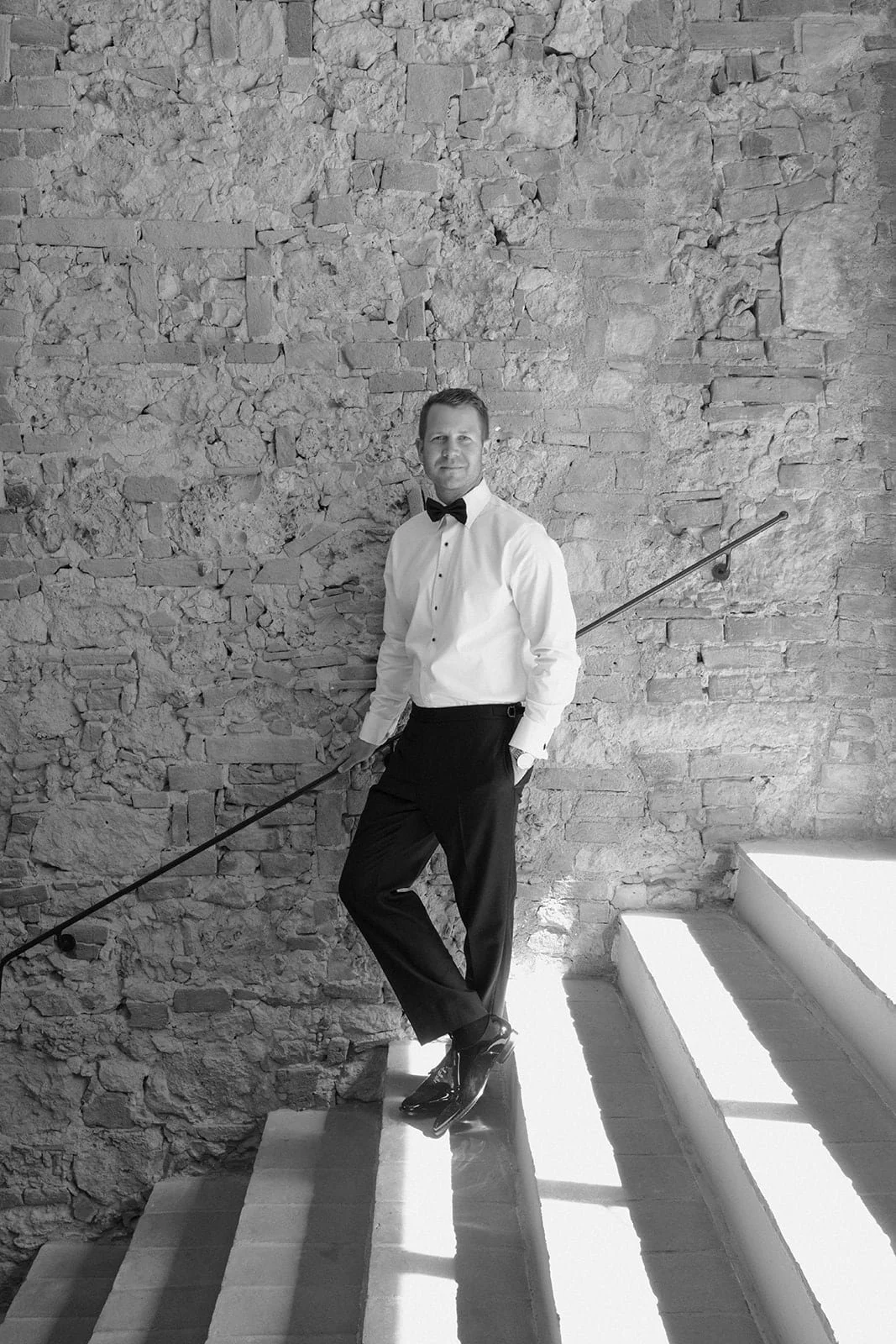 Black and white portrait of the groom on a stone staircase at Villa Lena, capturing timeless elegance and quiet confidence.