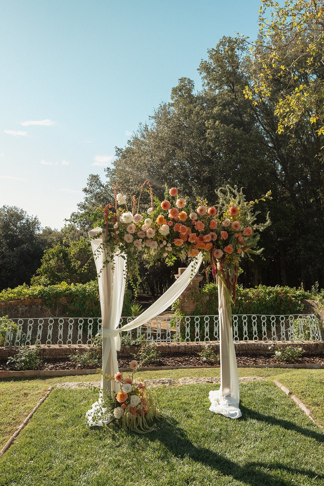A floral wedding arch decorated with seasonal blooms and fabric, set outdoors at Villa Lena for an intimate Tuscan ceremony.
