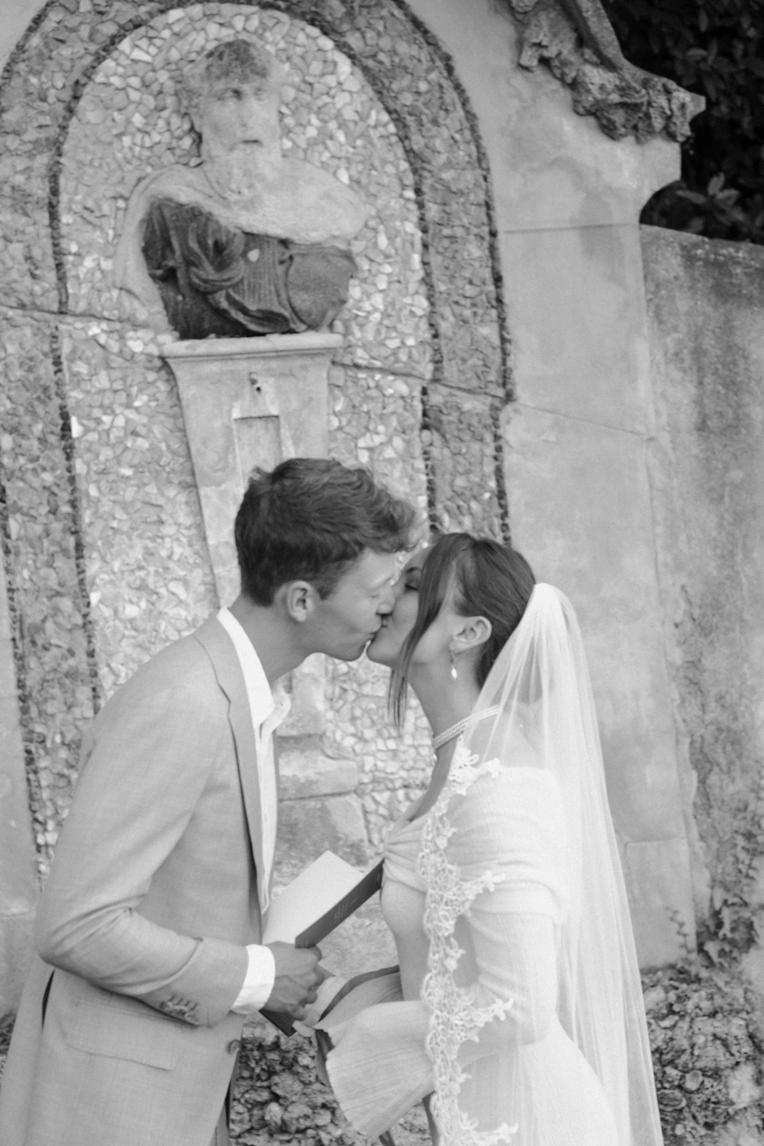 An intimate black and white elopement kiss in Florence, framed by historic stone architecture and classical sculpture for a timeless, editorial wedding moment.