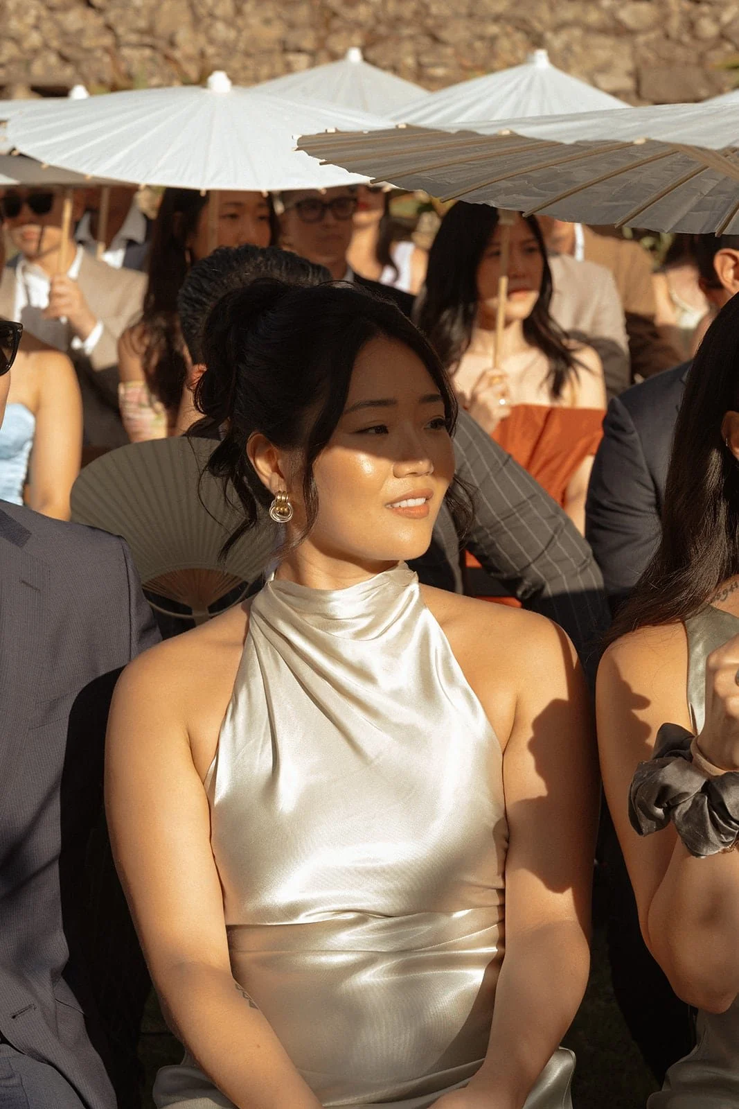 A close portrait of a guest seated during the ceremony, illuminated by golden sunlight and framed by parasols in the background.