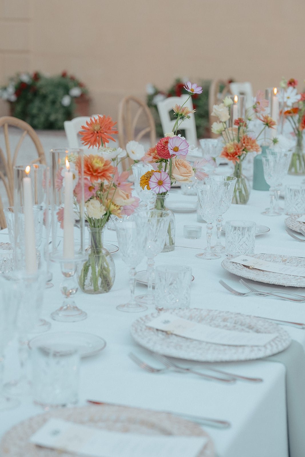 A bright, airy shot of the reception table setup, showcasing the mix of wooden cross-back chairs and white chairs against a backdrop of green garden hedges.