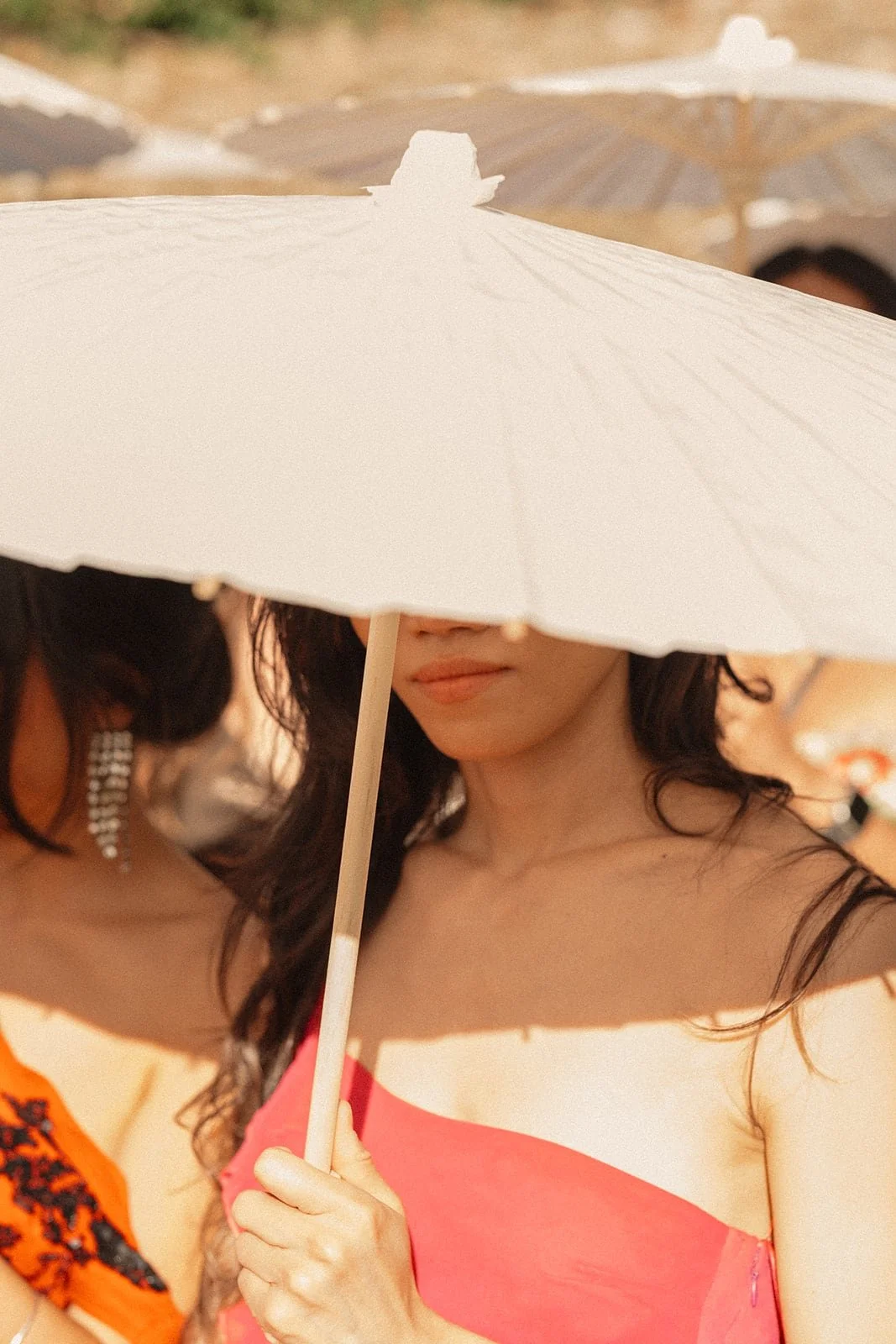 A wedding guest holds a white parasol under the summer sun, captured during an outdoor ceremony in the Tuscan countryside.