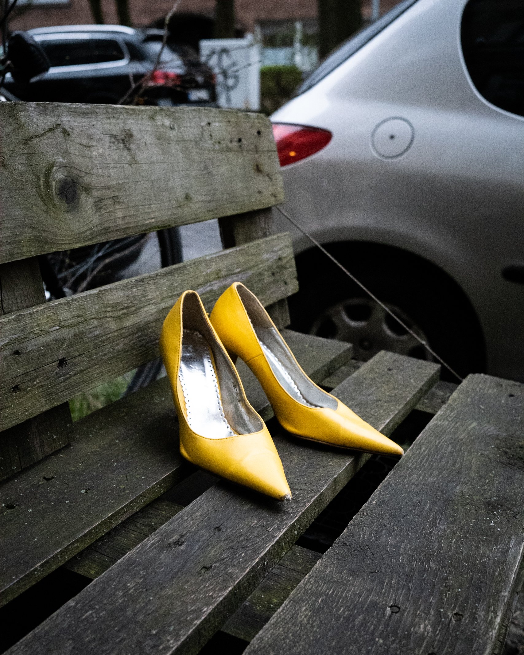 Gelbe High Heels auf einer Holzbank neben einem parkenden Auto.