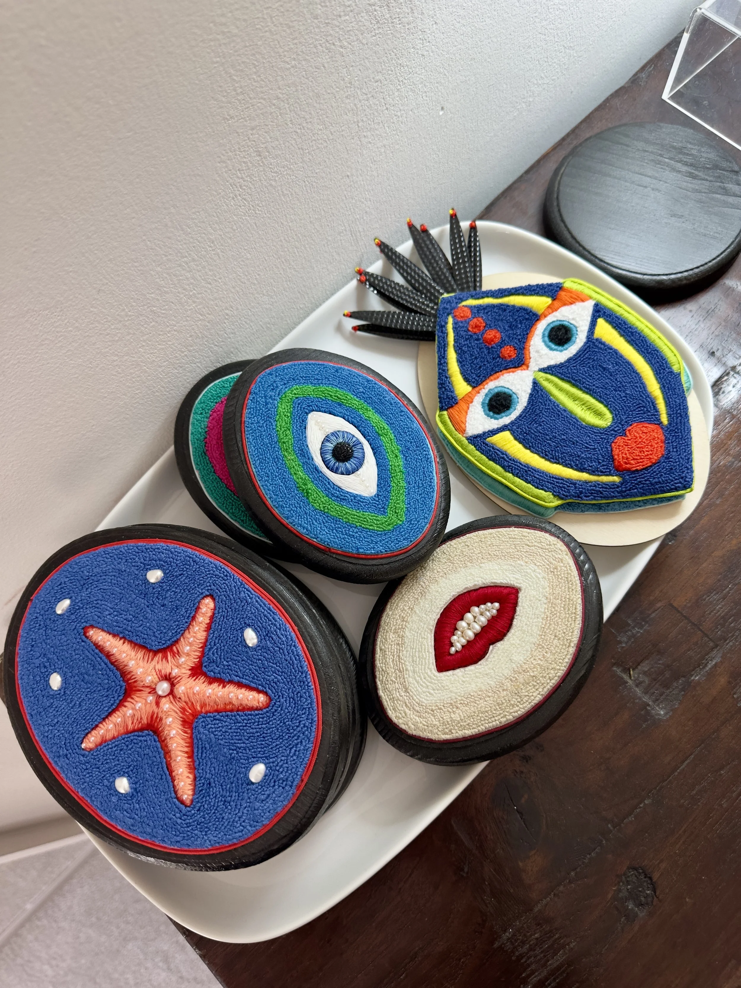 Colorful embroidered patches with ocean and face designs, displayed on a white tray.
