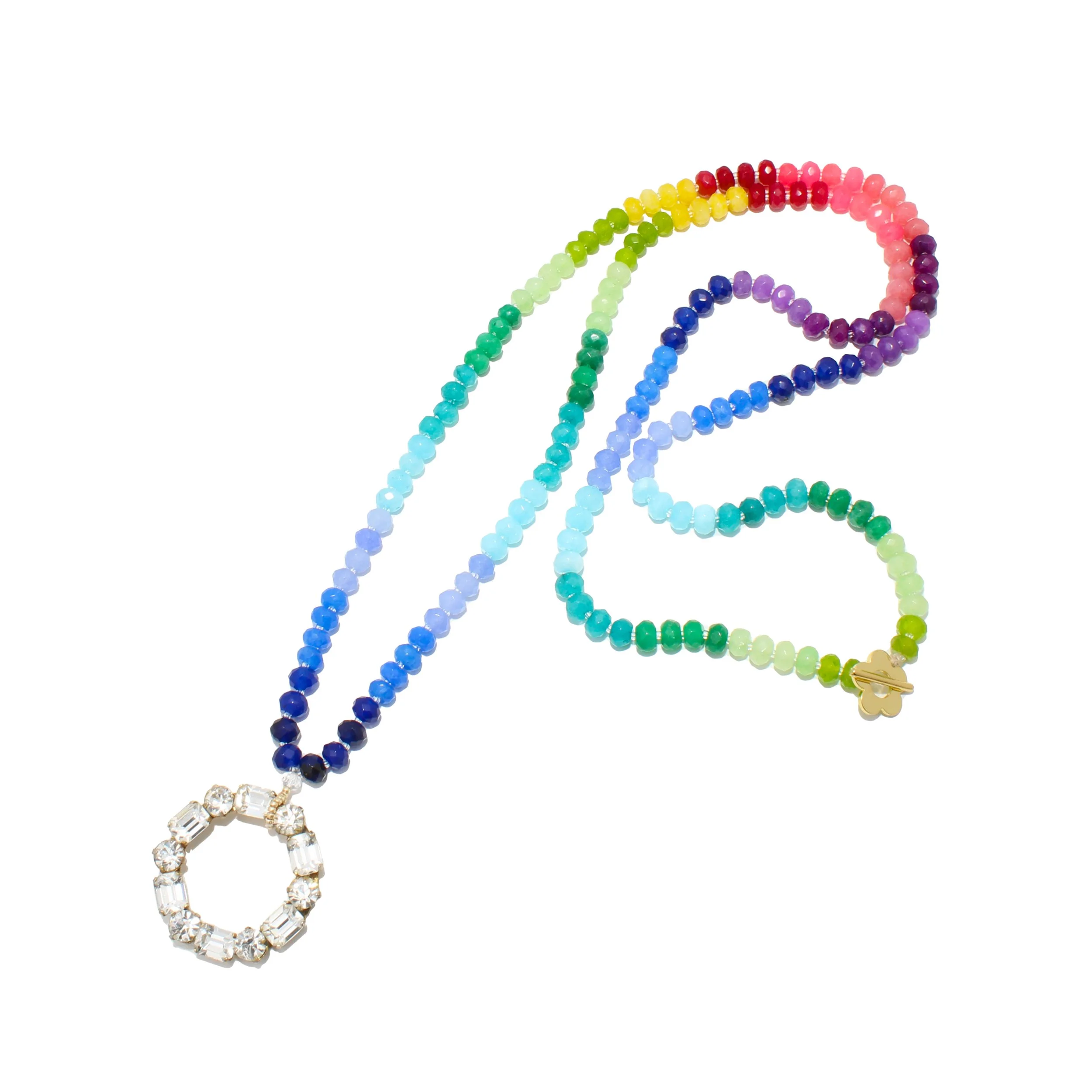 Colorful beaded necklace with rainbow beads and a pendant with clear stones, laid on white background.