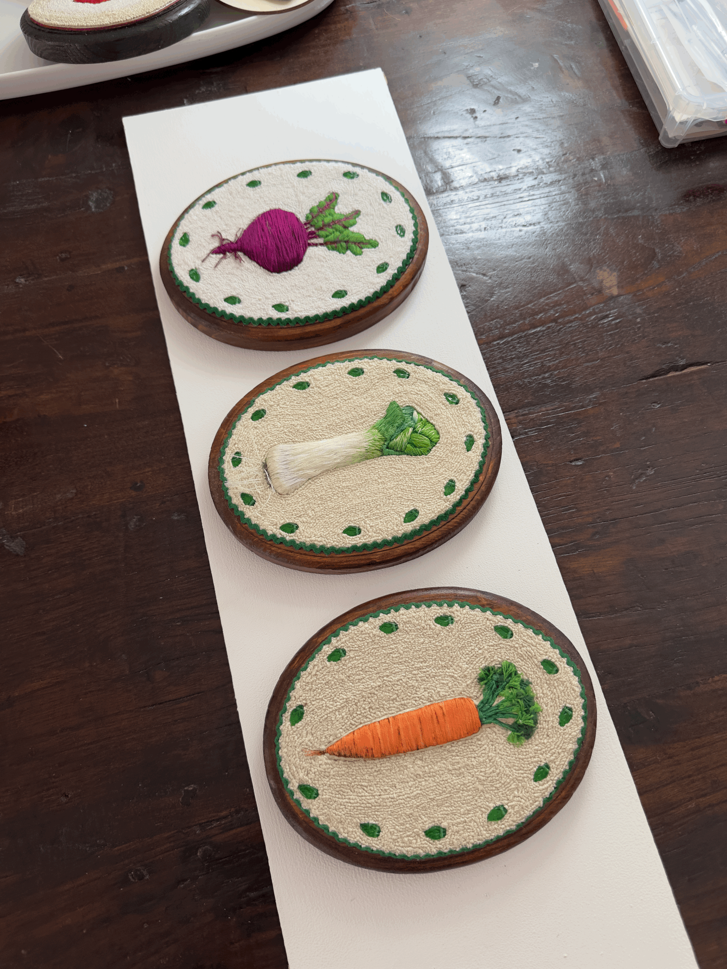 Three embroidered patches of vegetables: a beet, a bunch of green onions, and a carrot, arranged vertically on a white surface.