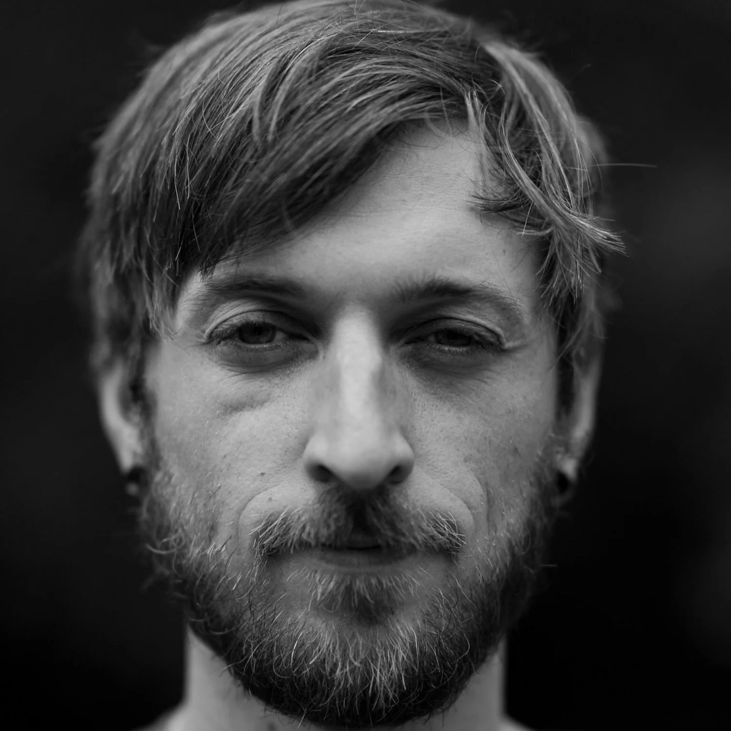 Black and white close-up portrait of a young man with medium-length hair and a beard.