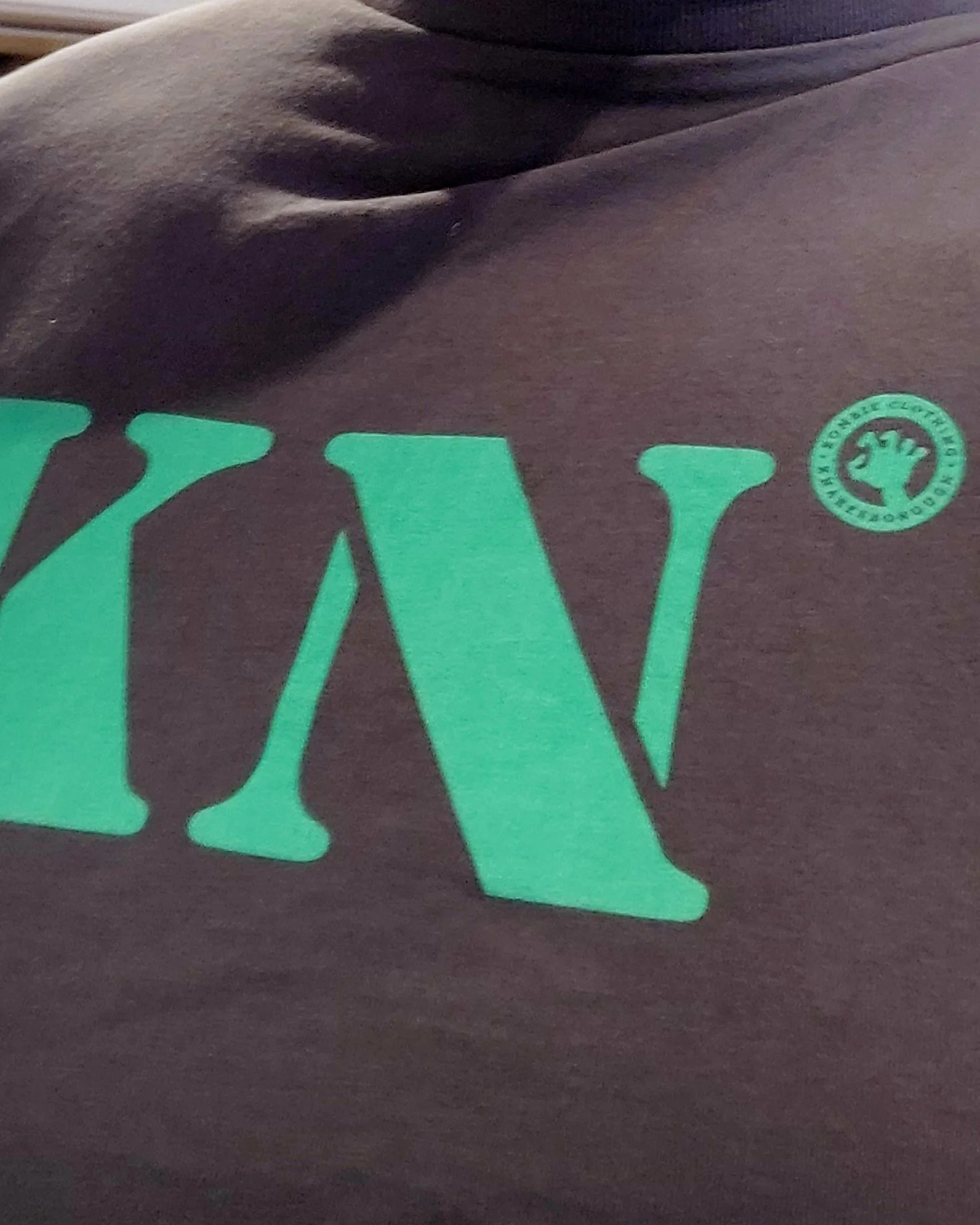 Close-up of a sweatshirt with green text and a logo on a dark fabric.