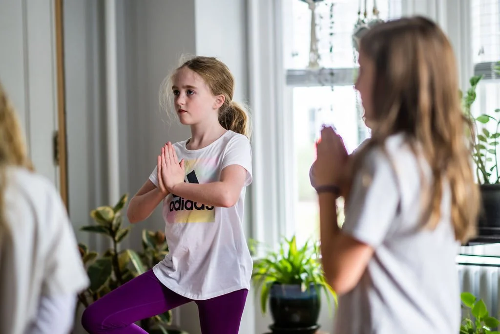 Young girl practicing yoga or meditation with others in a bright indoor space.