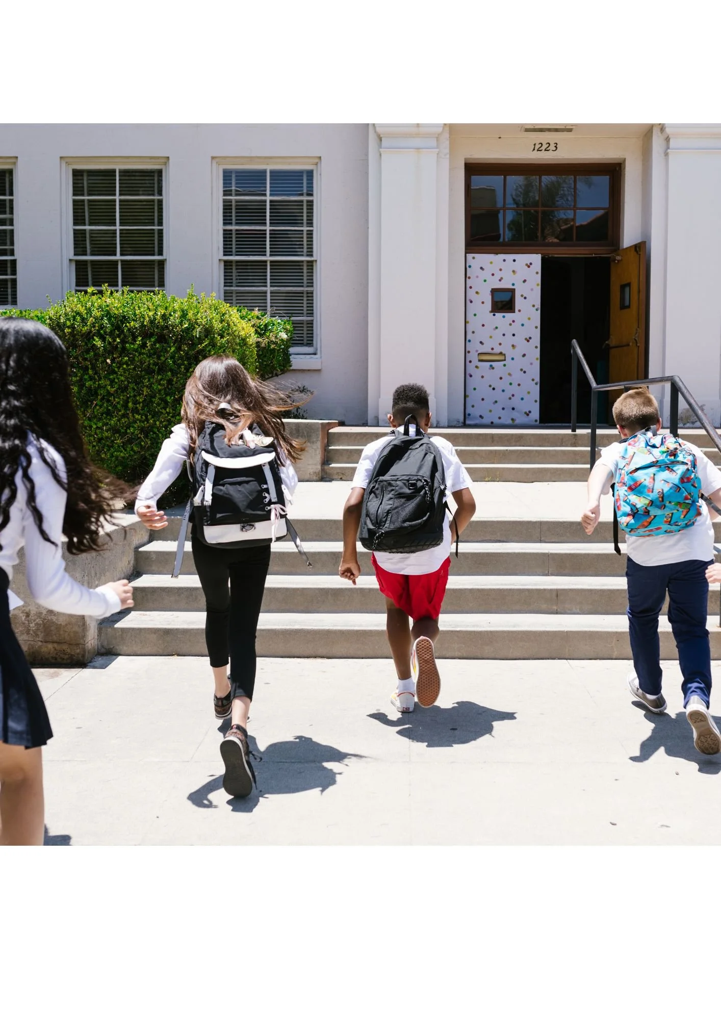 Kids with backpacks running up the stairs outside a school building.
