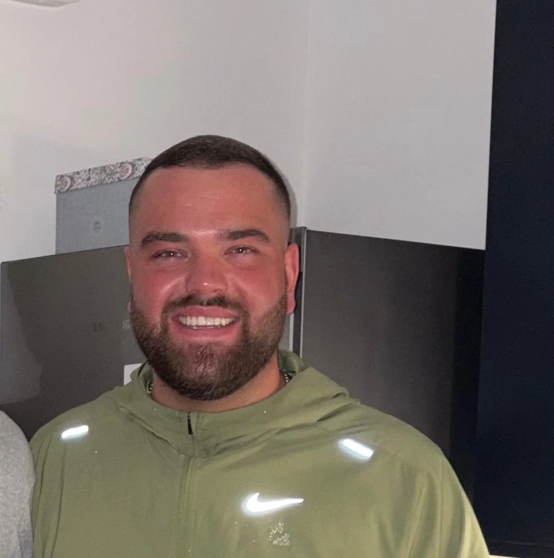 Person smiling indoors, wearing a blue shirt and dark jacket.