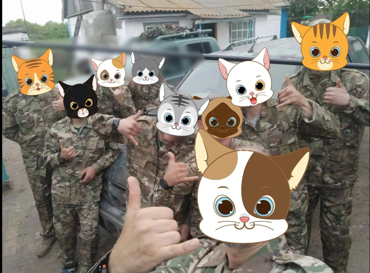 Group of people in camouflage with cartoon cat faces over their heads, posing with hand gestures.