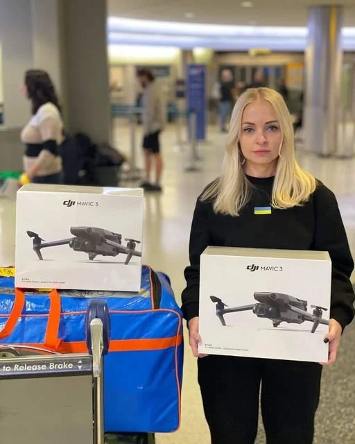 Woman at an airport holding DJI Mavic 3 drone boxes next to luggage cart.