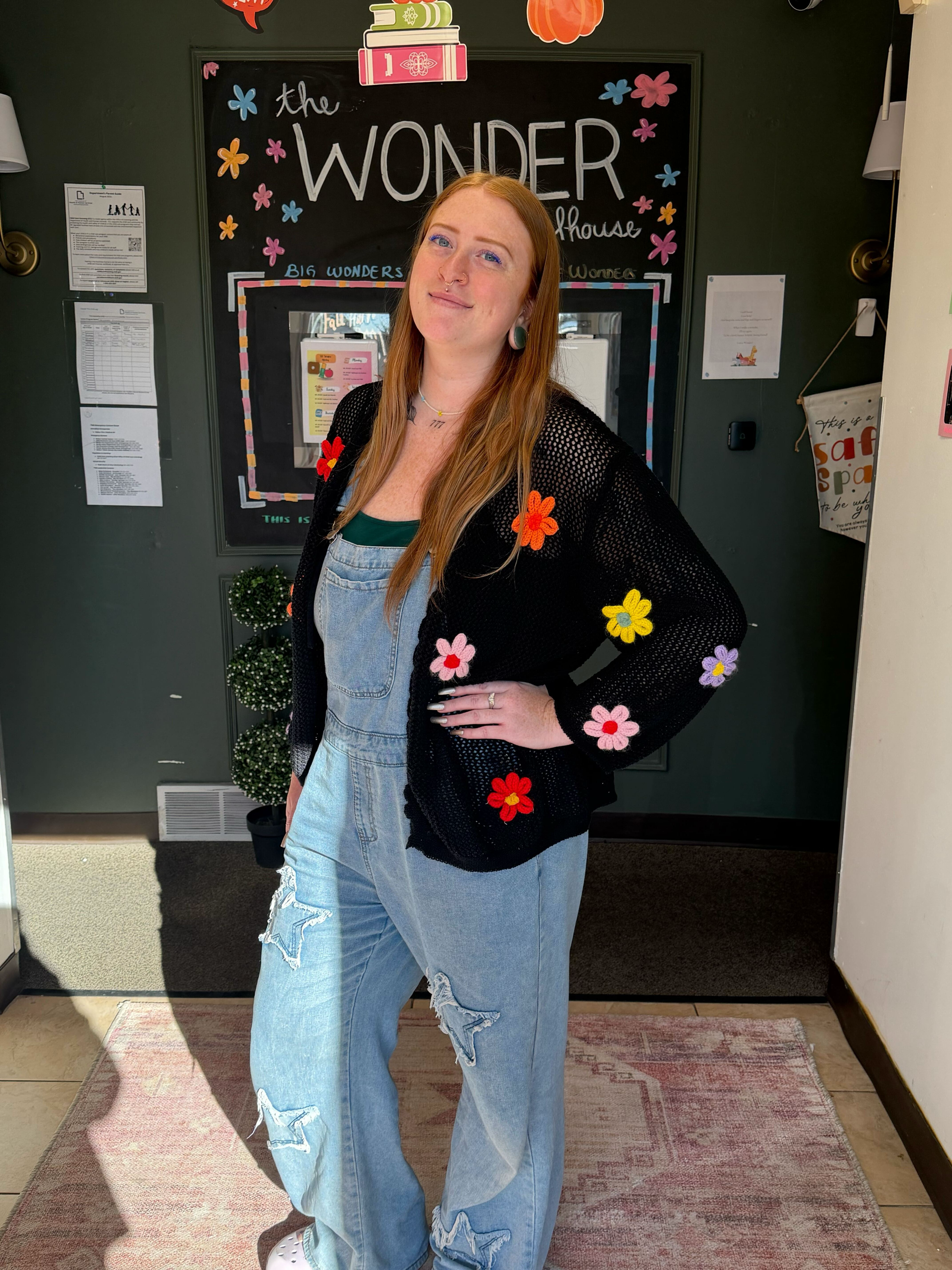 Close-up of a woman with long red hair, blue eyes, earrings, and a small nose ring in a cozy living room.