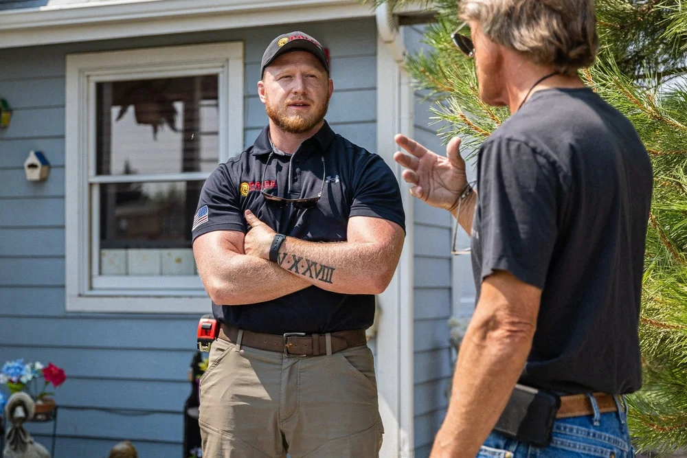 A Pride Roofing representative listens to a homeowner outside the house.