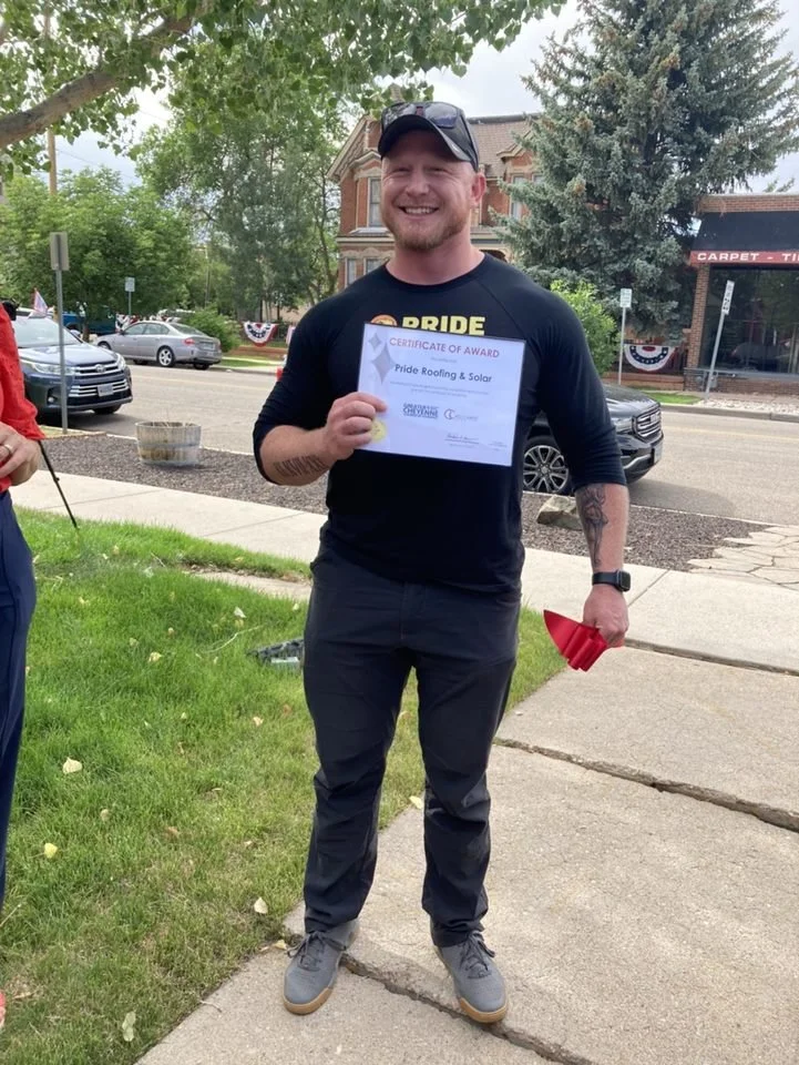 Man in a Pride Roofing Shirt and Hat Holding a Ribbon Cutting Award for the City of Cheyenne Wyoming