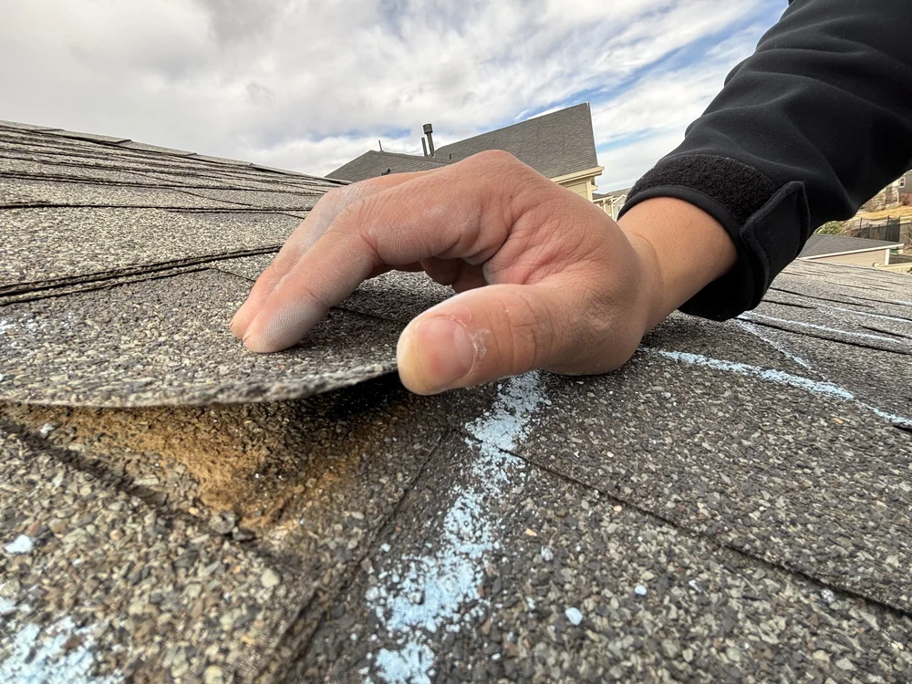 A Pride team member lifts a damaged shingle to inspect the roof’s condition.