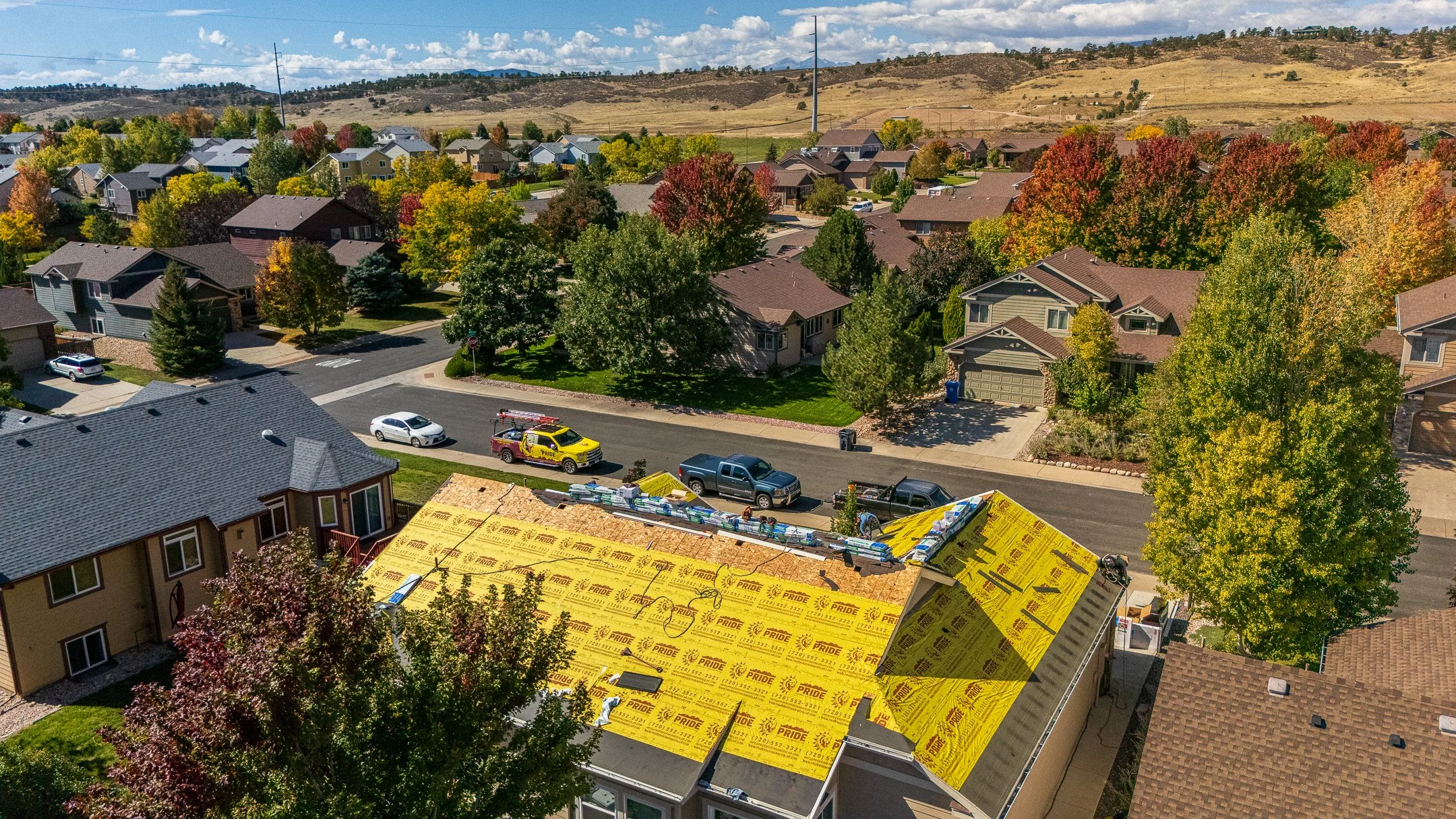 Aerial view of suburban houses next to a golf course with lakes, trees, and open land.