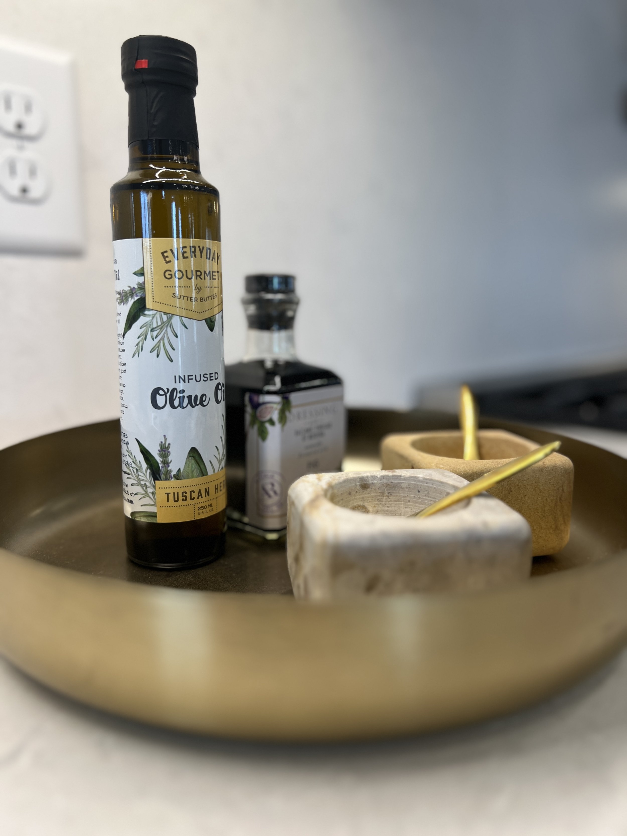 A coffee brewing setup on a wooden tray with a glass Chemex coffee maker, a white mug with the phrase 'enjoy the journey,' a small potted succulent, a jar of coffee beans, and a white wall with electrical outlets in the background.
