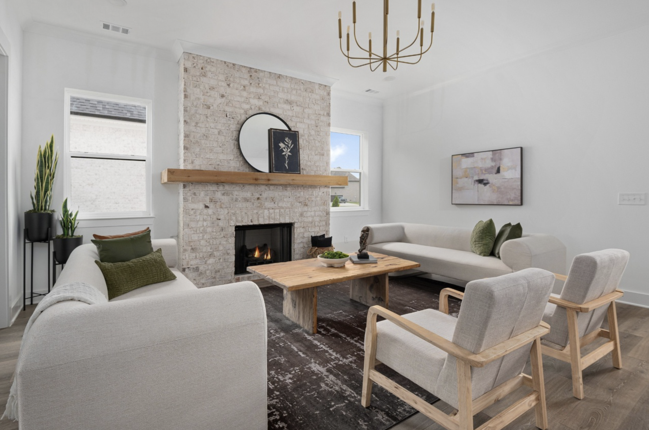 Living room with a brick fireplace, white walls, modern furniture, a wooden coffee table, a fireplace with a fire burning, abstract artwork on the wall, and indoor plants.