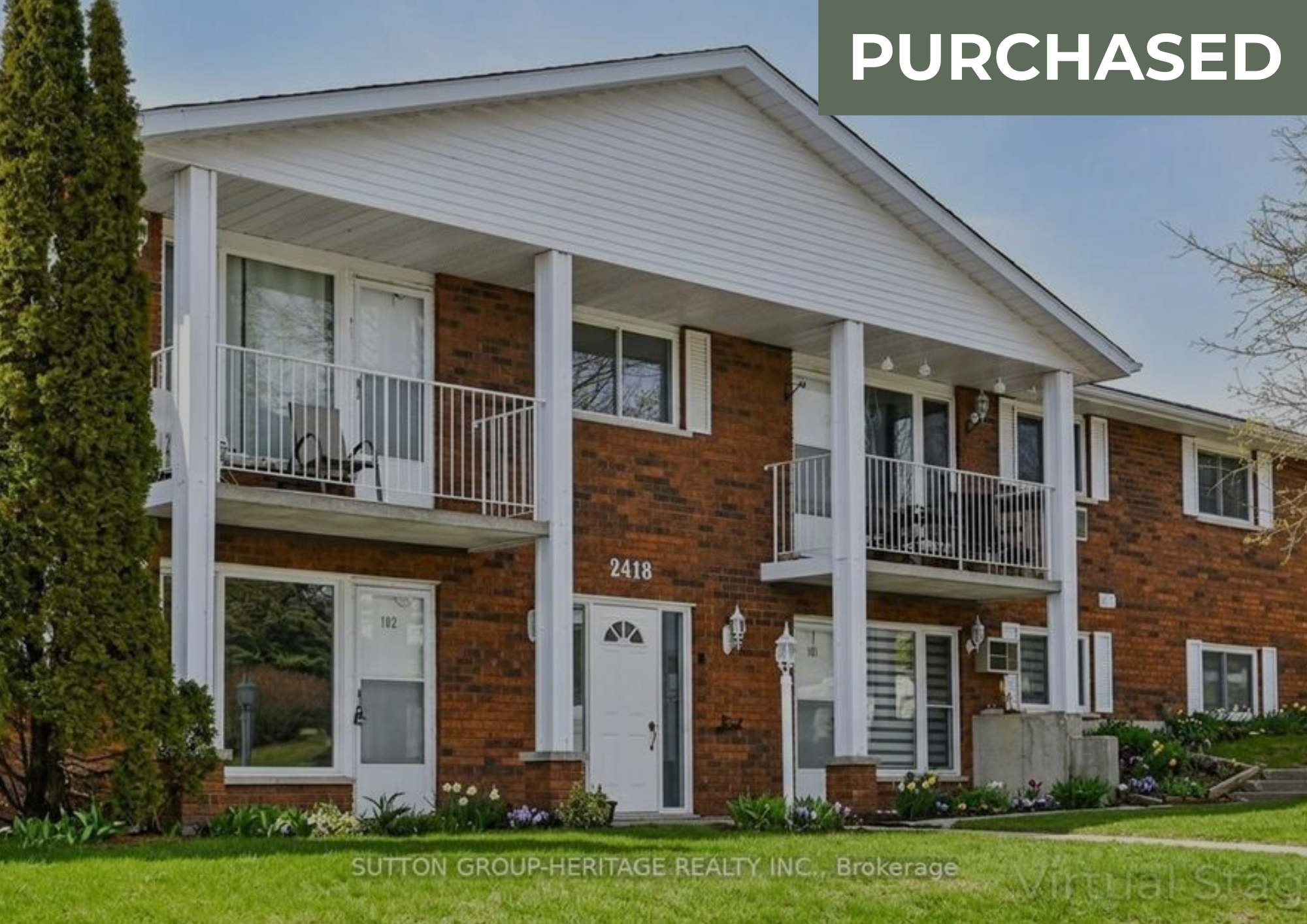 A multi-story brick apartment building with white balconies and a well-maintained lawn with flowers, newly purchased as indicated by the "PURCHASED" banner.