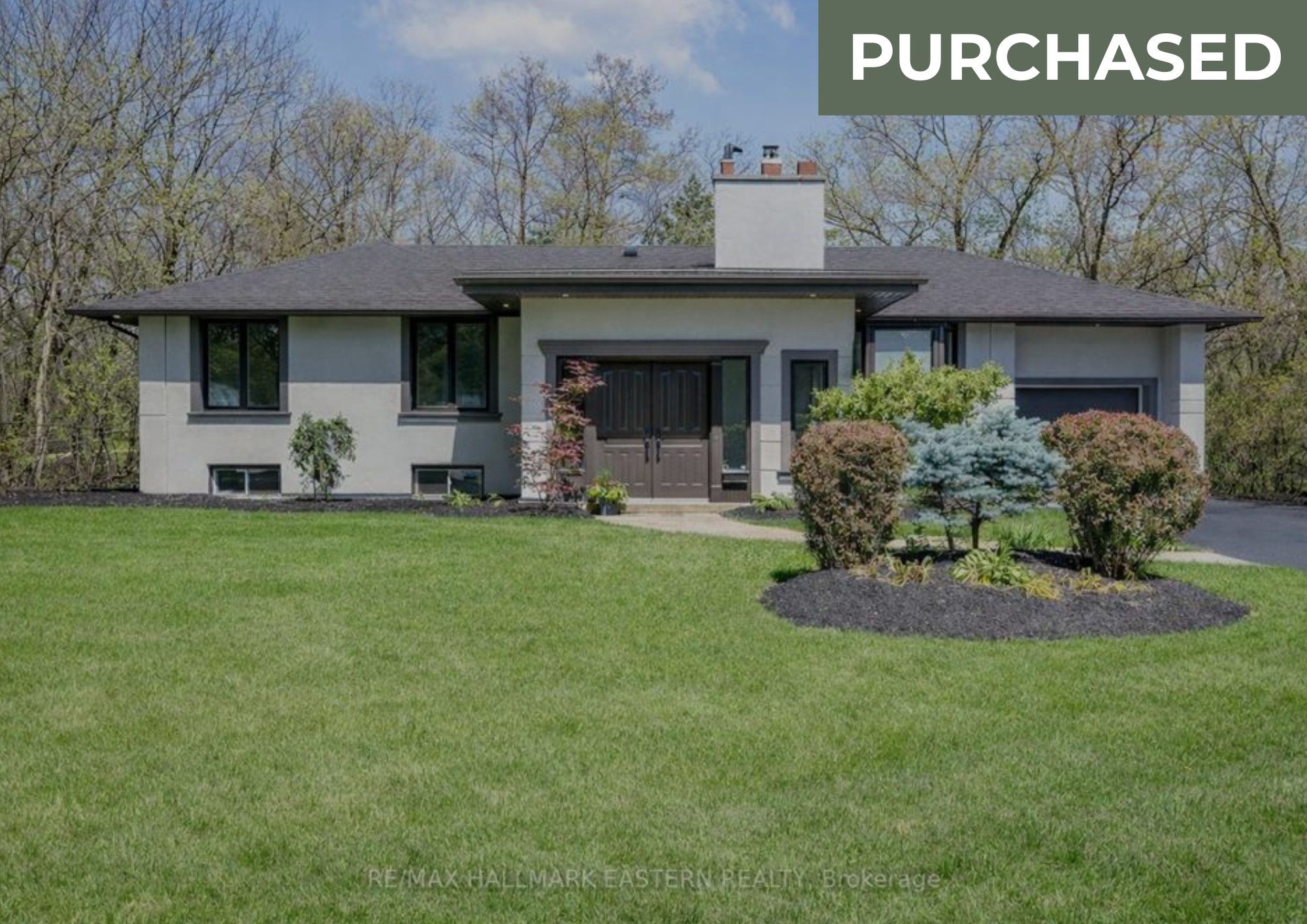 Front view of a modern house with a manicured lawn, shrubs, and trees in the background, and a "PURCHASED" label in the upper right corner.