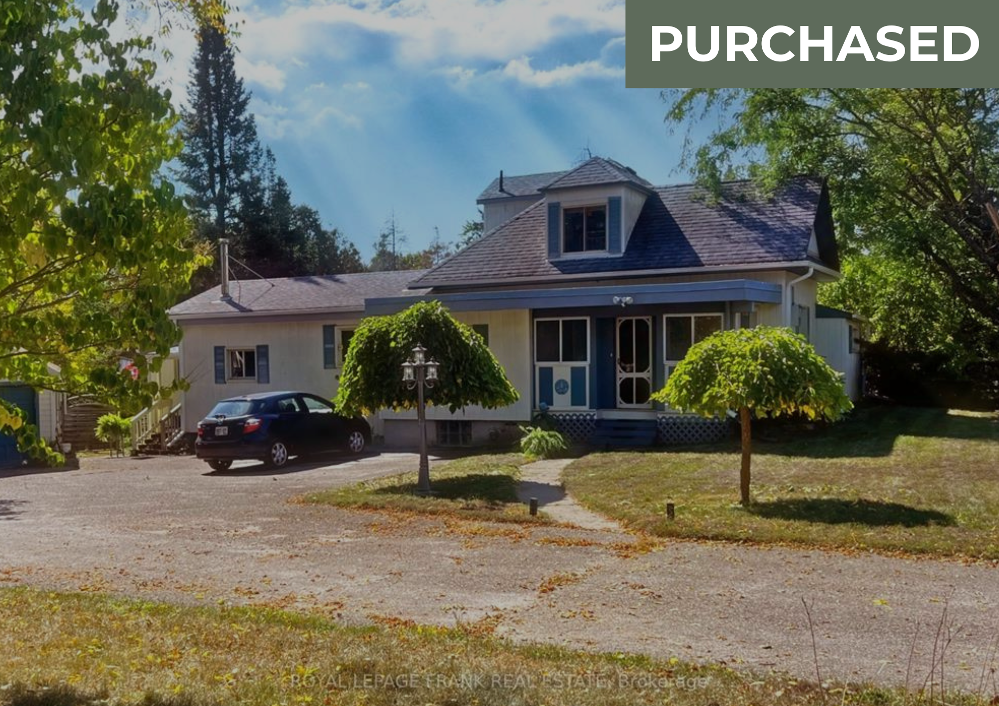 Front view of a blue house with trees and a parking lot, marked as purchased.