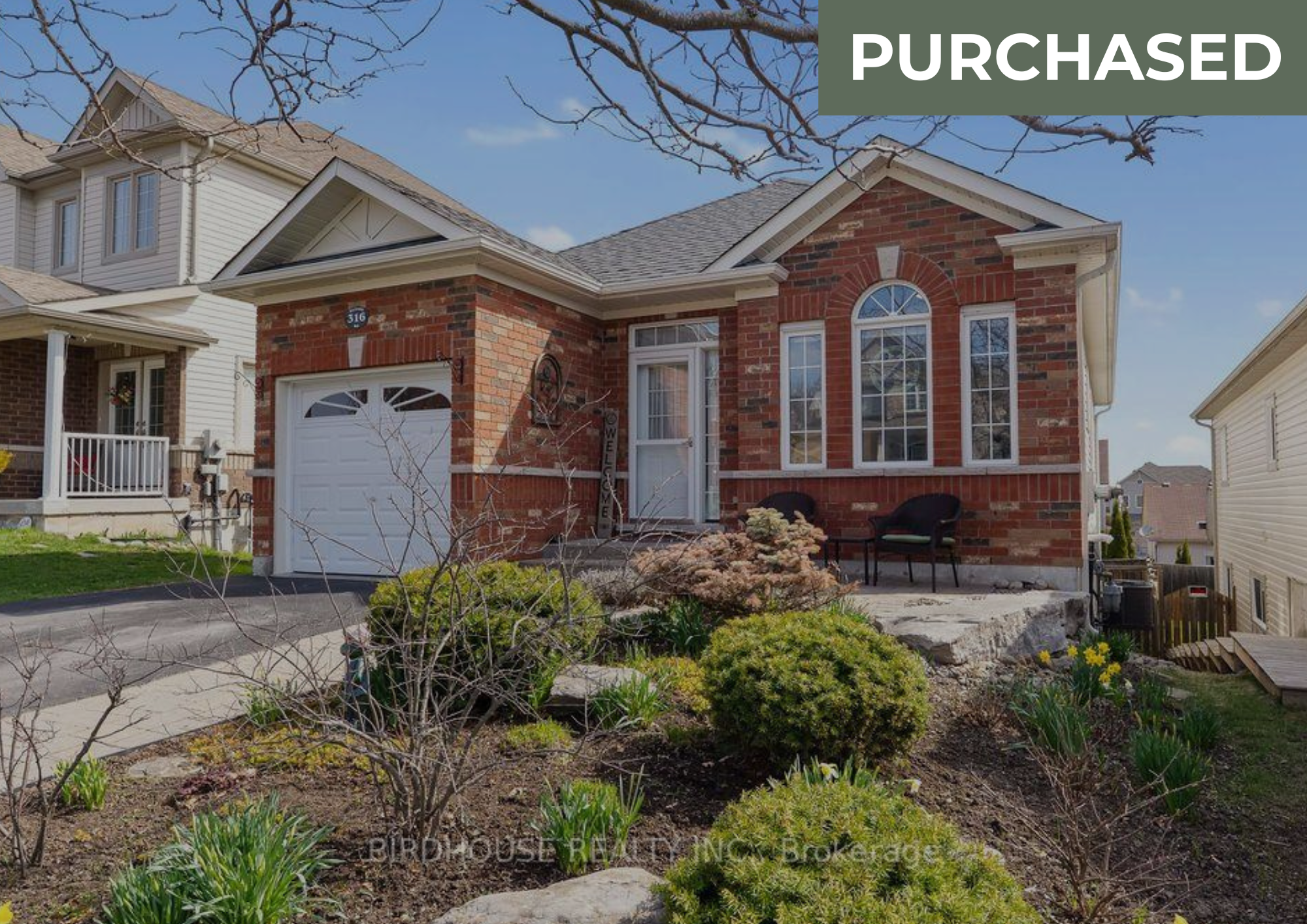 Front view of a brick and siding house with a white garage door, a small front porch, garden, and a "purchased" label.