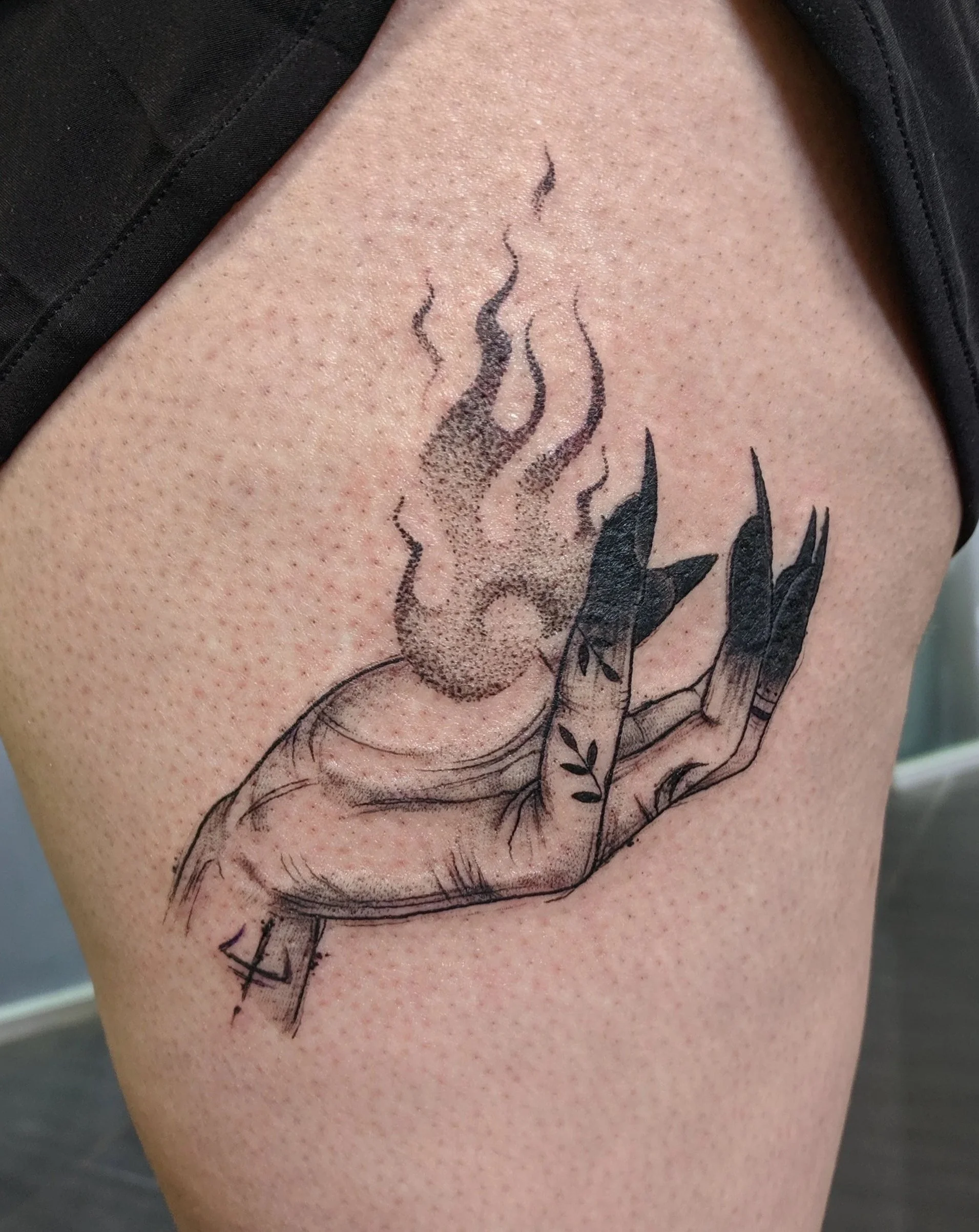 A tattoo of a hand with long, pointed nails, with a fire ball on a person’s thigh