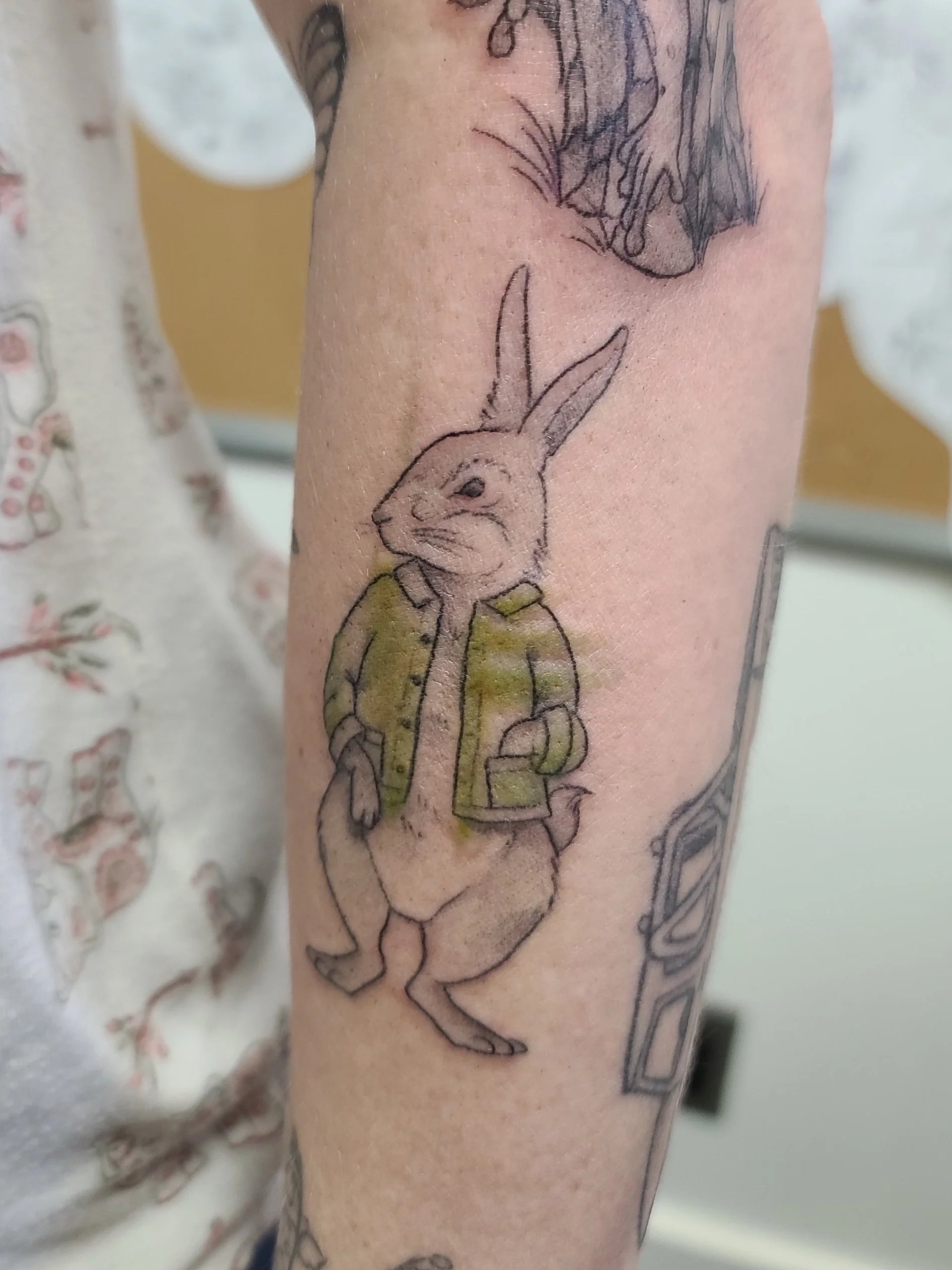 A tattoo of a rabbit wearing a green jacket on a person's arm.