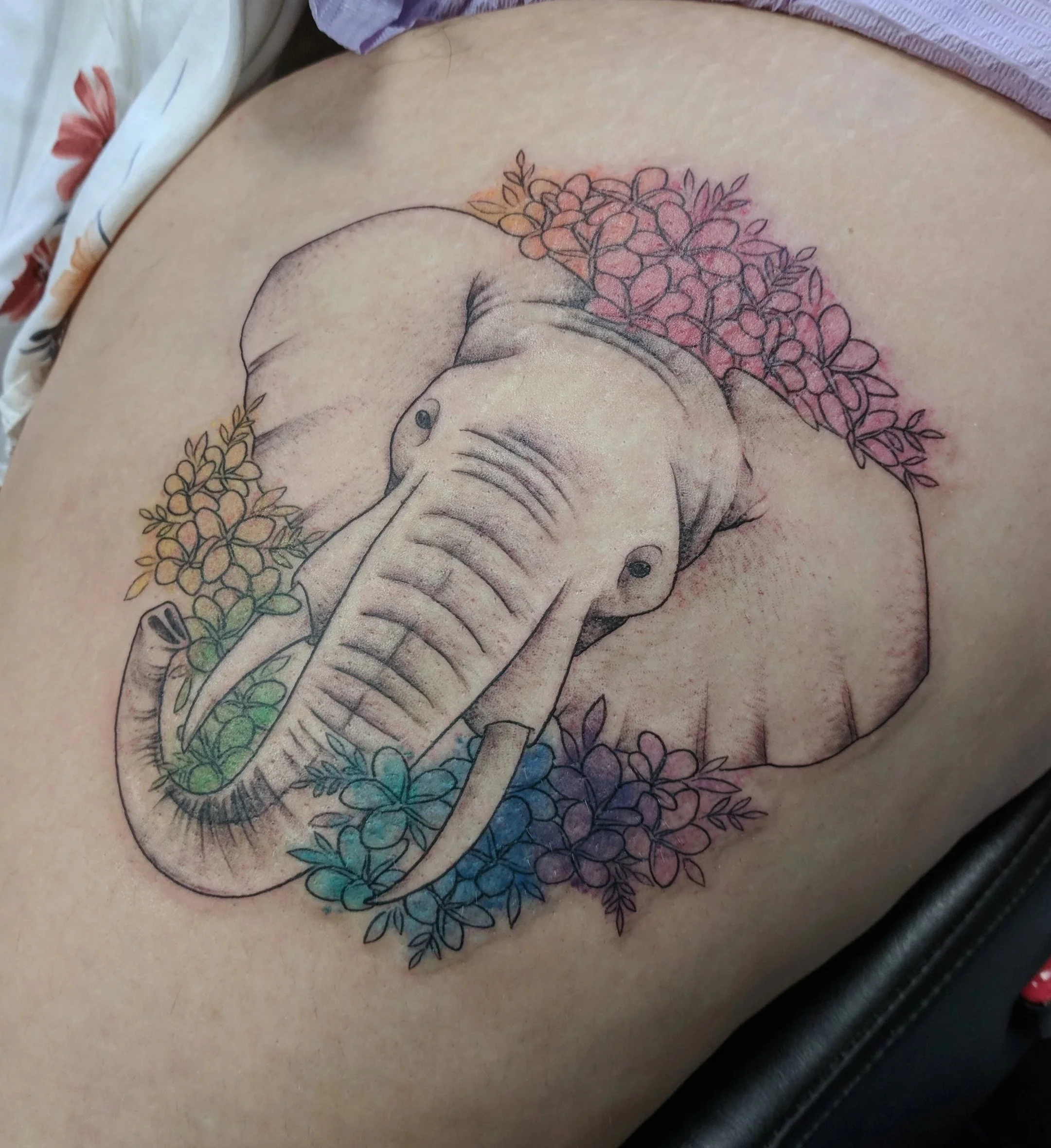 Tattoo of an elephant surrounded by colorful flowers on a person's skin.