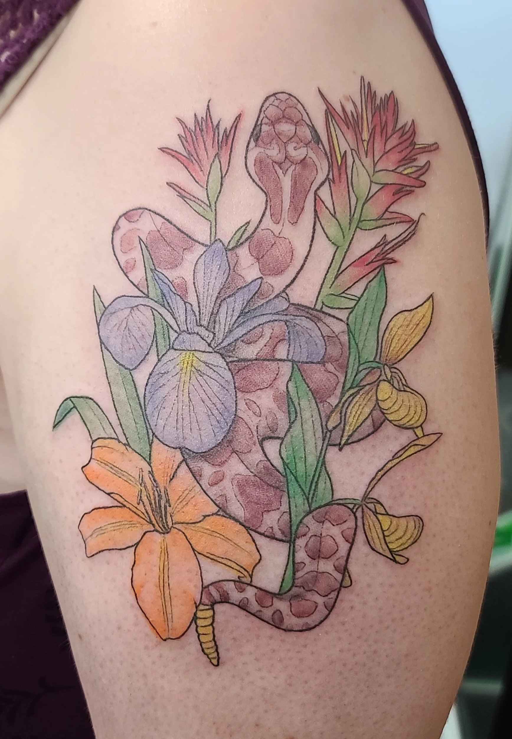 A colorful tattoo of a snake intertwined with flowers, including irises and lilies, on a person's upper arm.