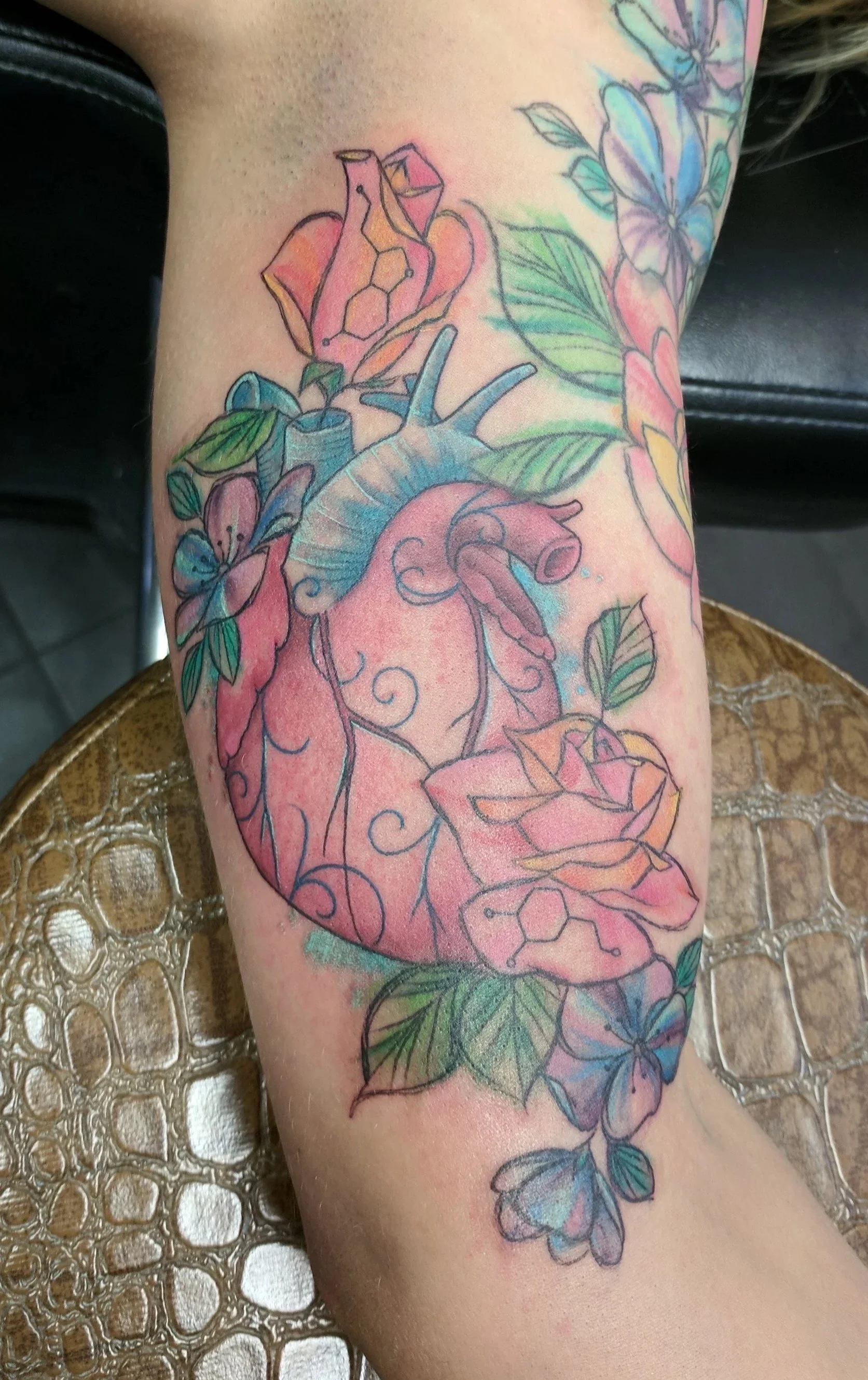 Colorful tattoo of an anatomical heart with flowers and leaves on a person's arm.