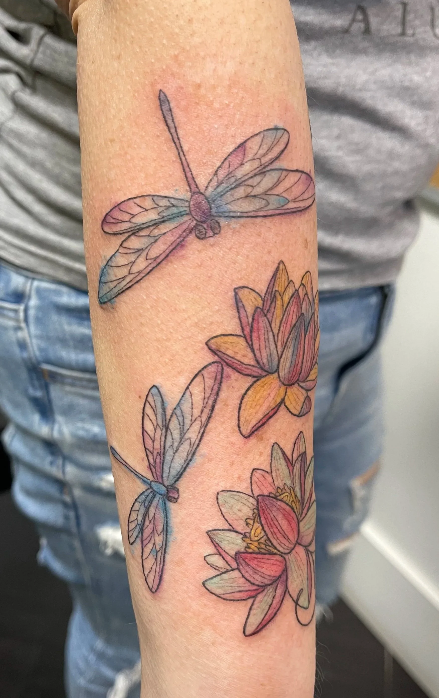 Tattoo of two dragonflies and three water lilies on a person's forearm.