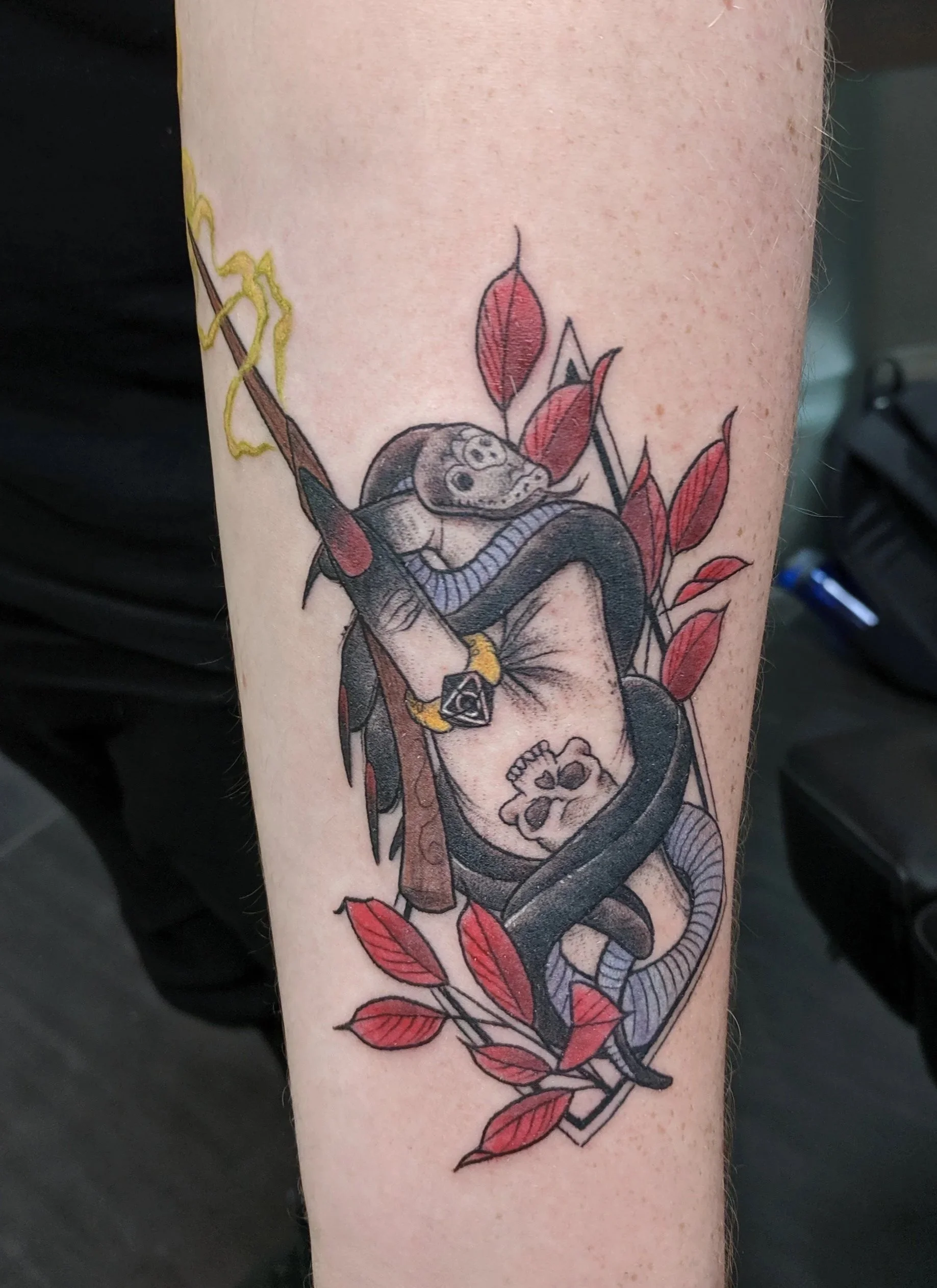 Tattoo of a snake coiled around a cup with a skull inside, surrounded by red leaves.