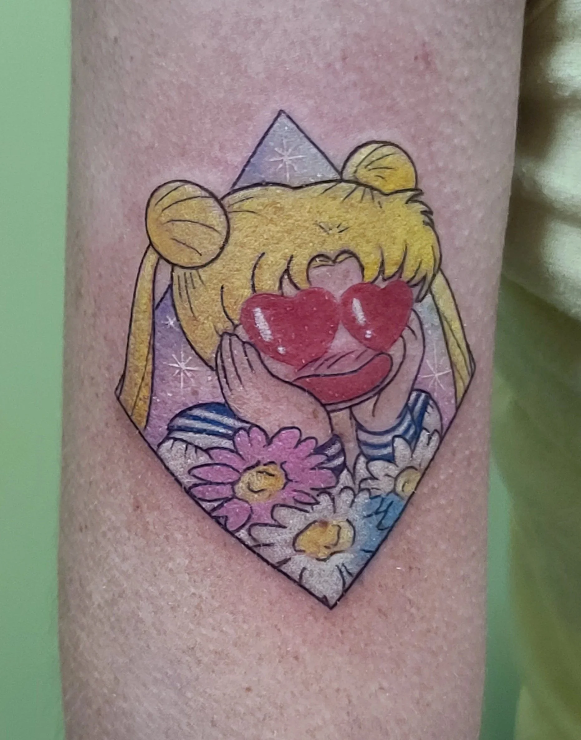 Tattoo of a cartoon girl with blonde hair and heart-shaped sunglasses, holding her cheeks, surrounded by flowers.