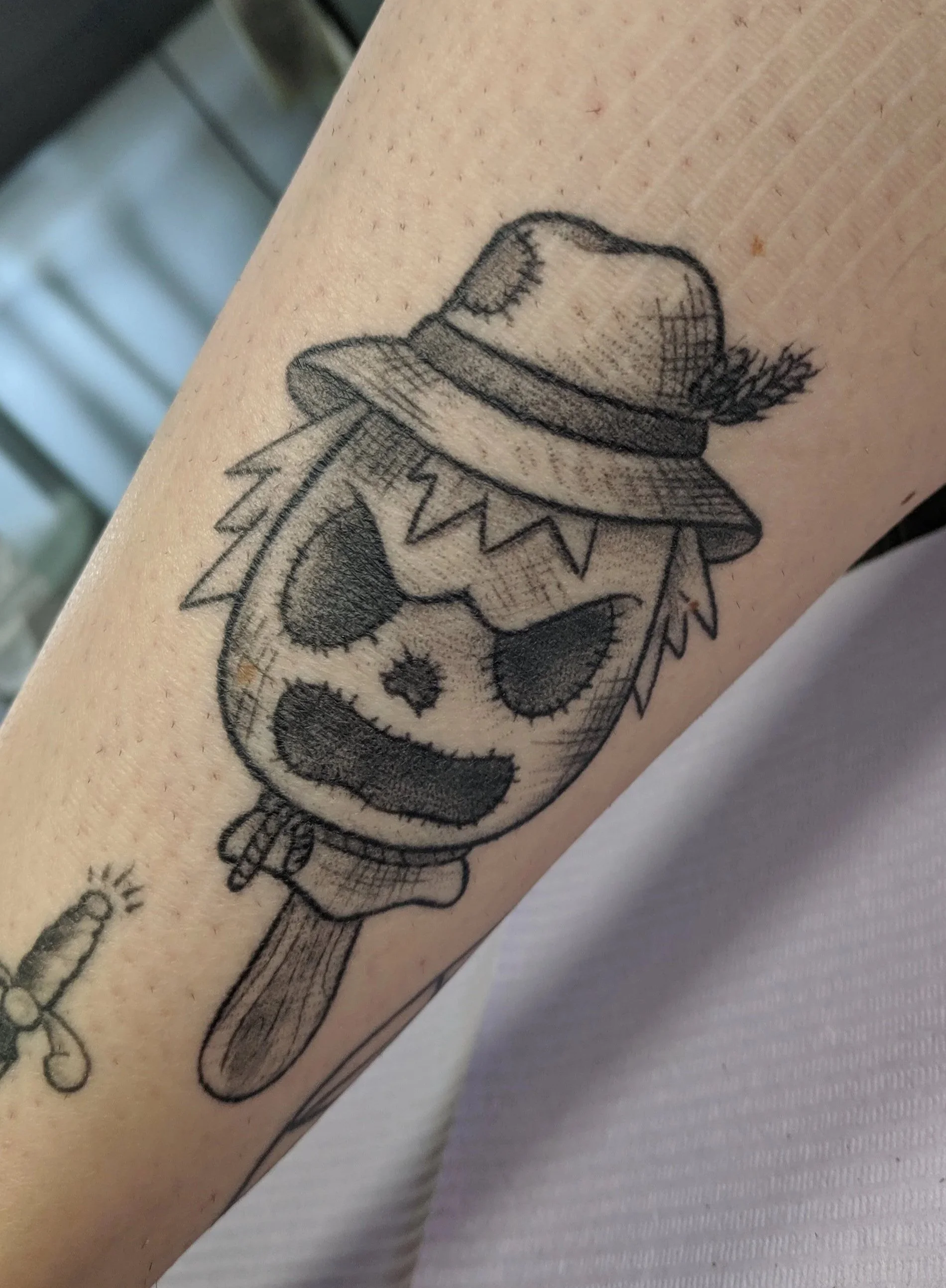Tattoo of a panda with a large head, wearing a wide-brimmed hat, and a scarf around his neck. The panda has a grumpy expression and is holding a fishing rod.