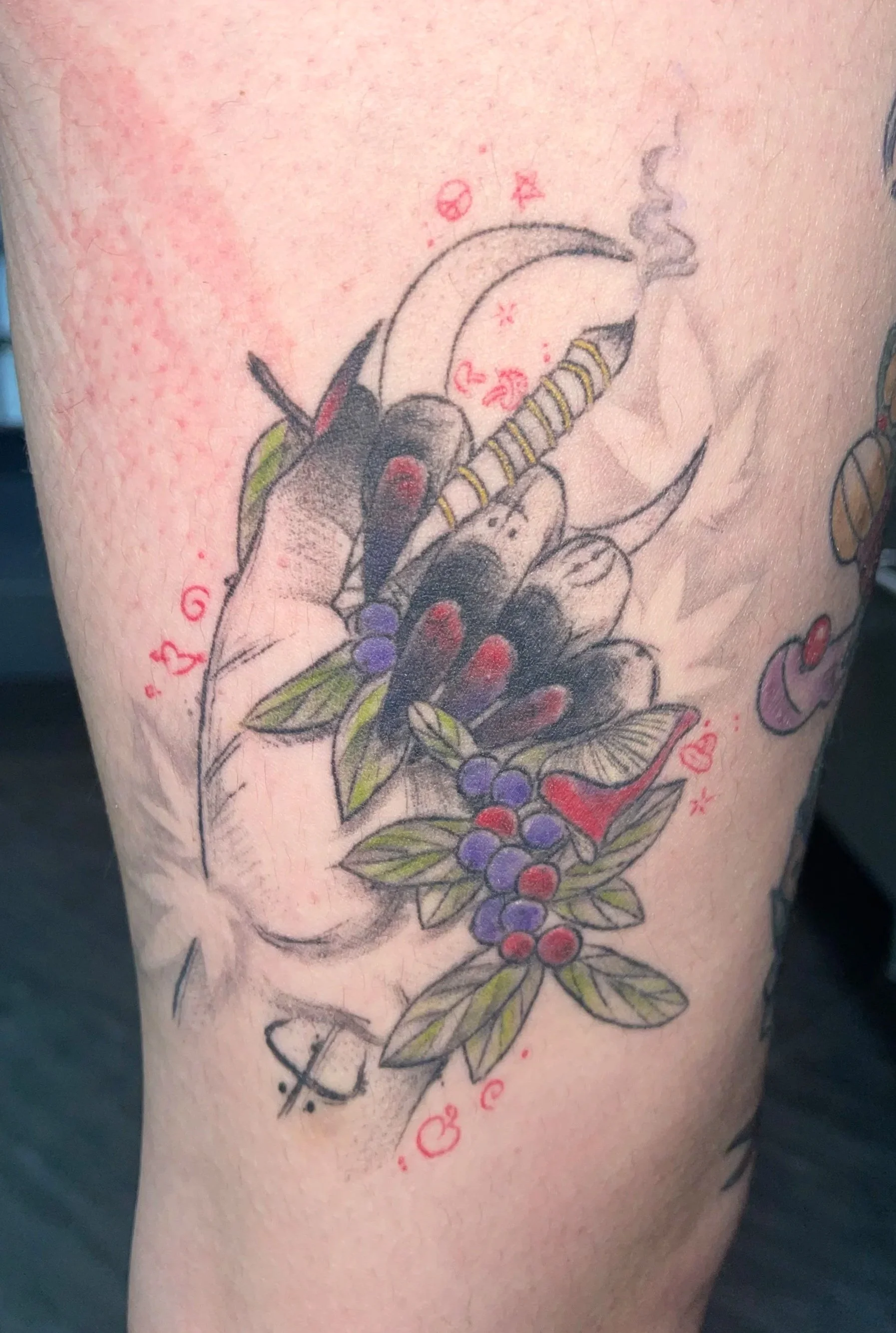 Tattoo of a bow with cherries, leaves, and decorative elements on person's thigh.