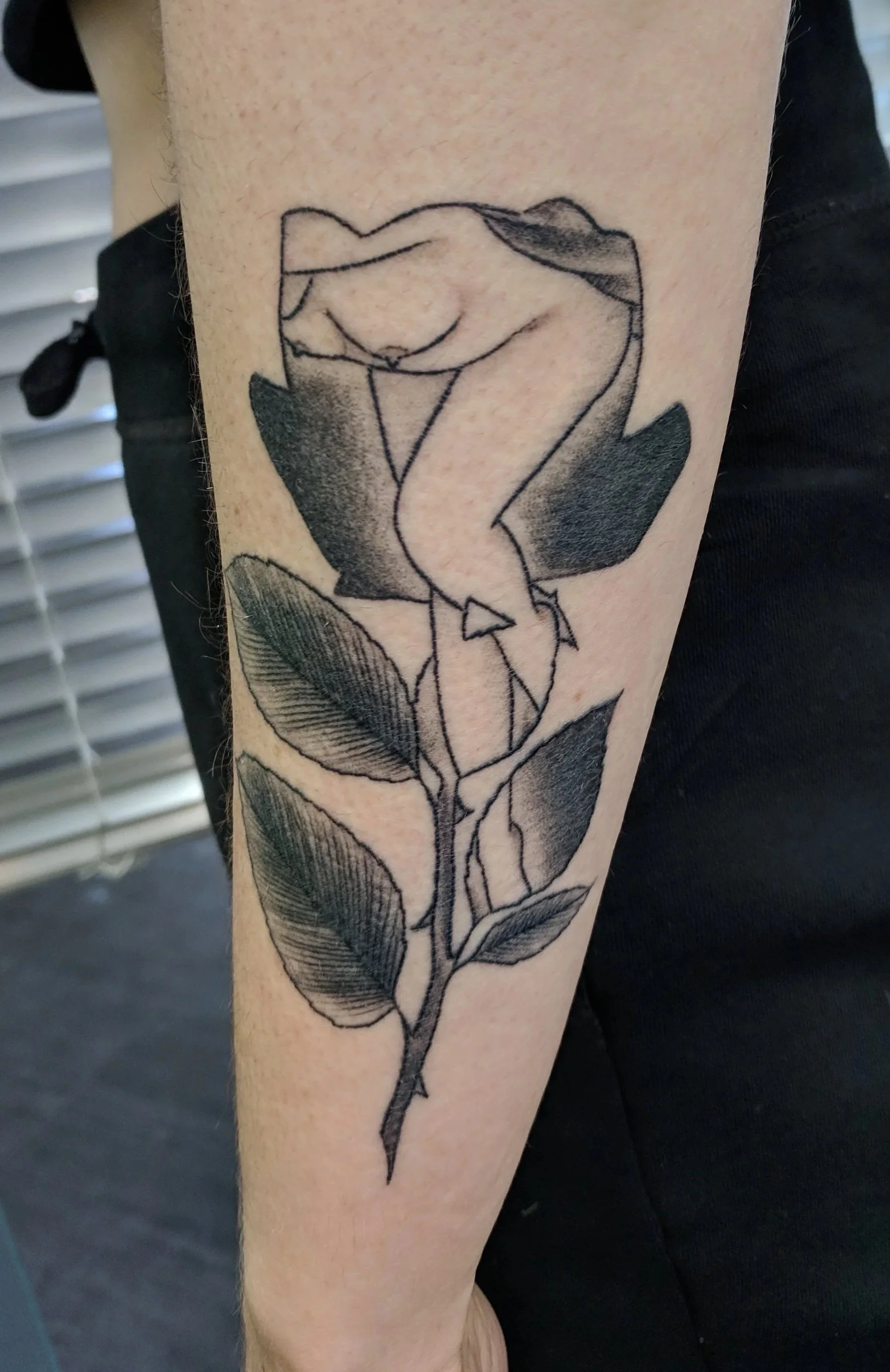 A black ink tattoo of a minimalist line drawing of a rose on a person's forearm.