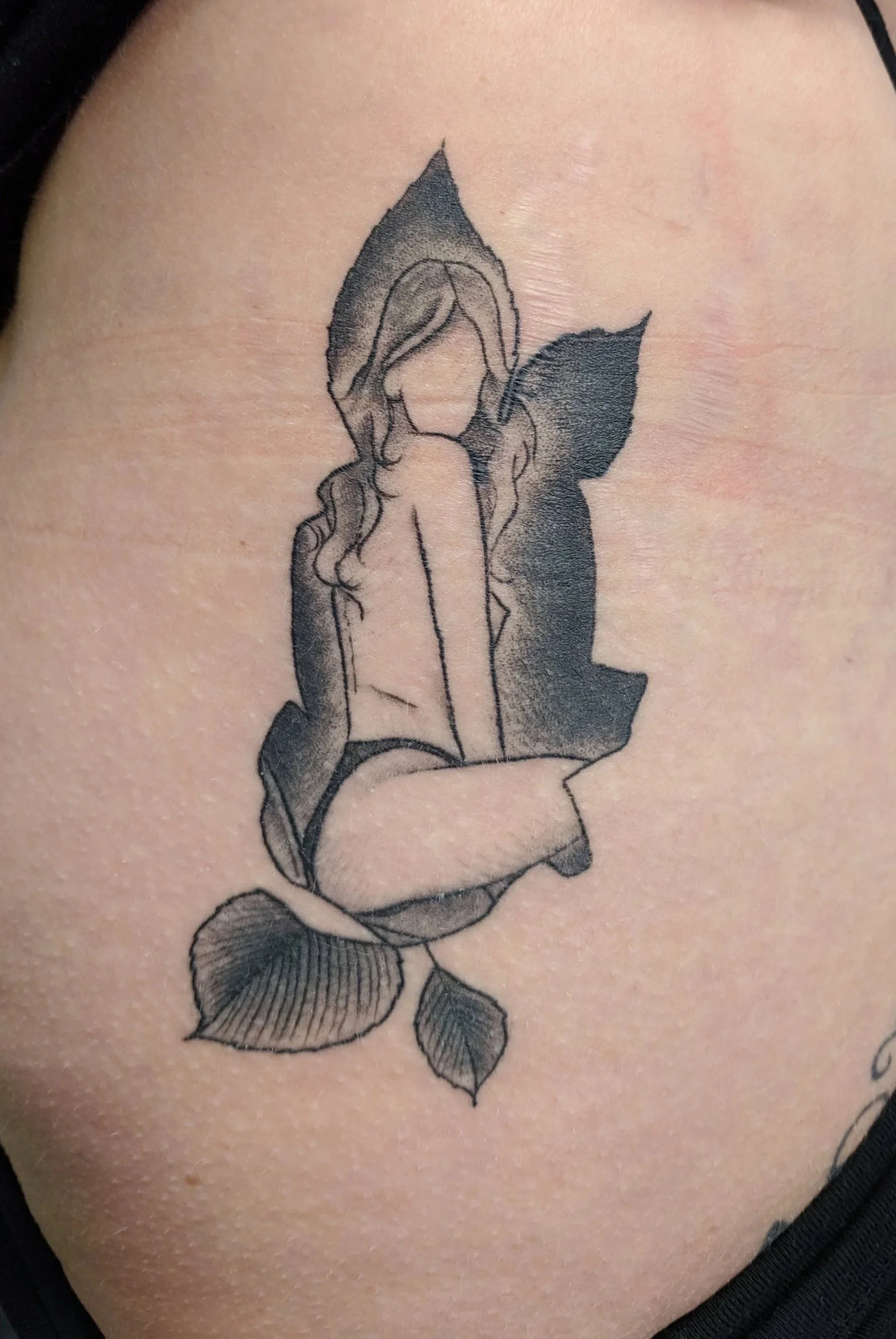 Tattoo of a woman with long hair, sitting inside a stylized rose with leaves, on a person's upper side.